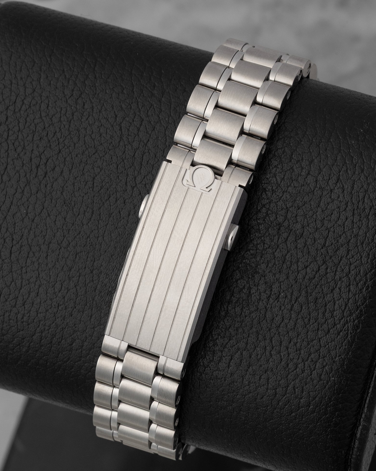 A rear view of the five-row stainless steel bracelet focusing on the brushed folding deployment buckle detailed with polished stripes and an embossed Omega emblem