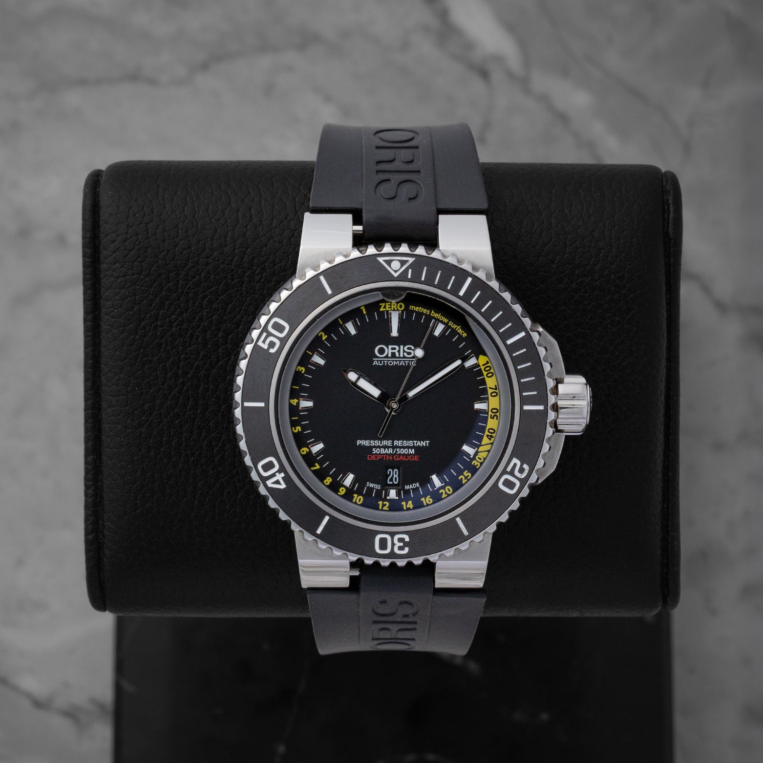 Pre-owned Oris Aquis Depth Gauge reference 01 733 7675 4154 featuring a black dial with yellow gauge channel scale and black rubber strap on display stand.