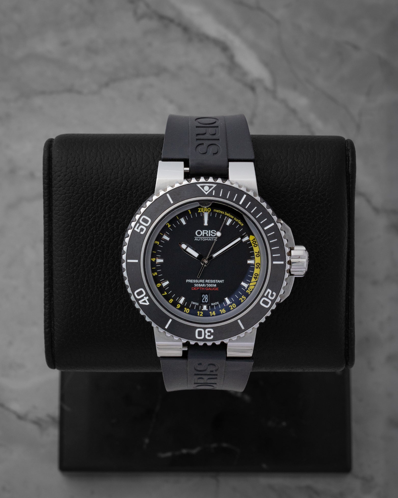 Pre-owned Oris Aquis Depth Gauge reference 01 733 7675 4154 featuring a black dial with yellow gauge channel scale and black rubber strap on display stand.