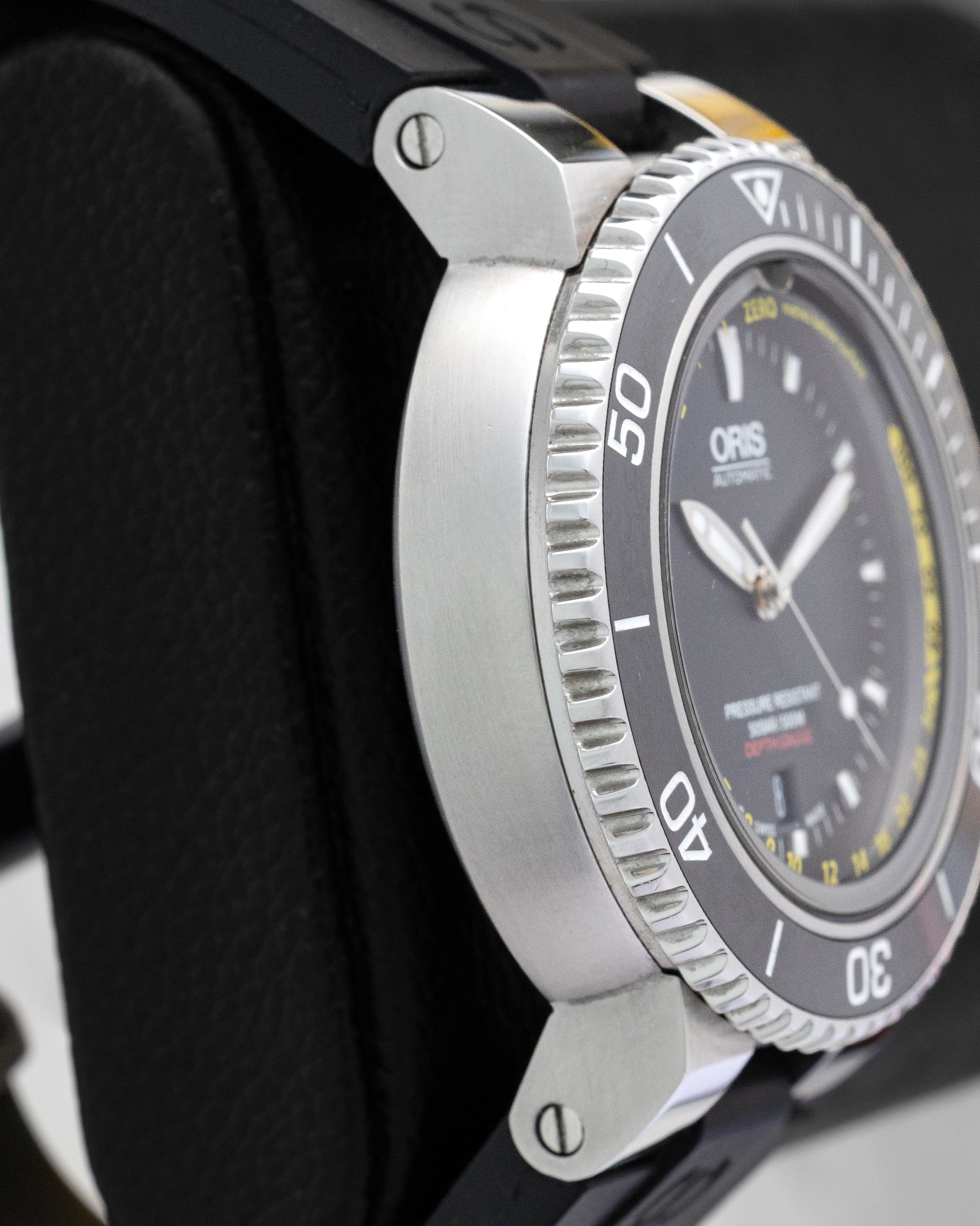 Left side profile view highlighting the thick stainless steel case, sapphire crystal depth entry hole, and knurled ceramic dive bezel.