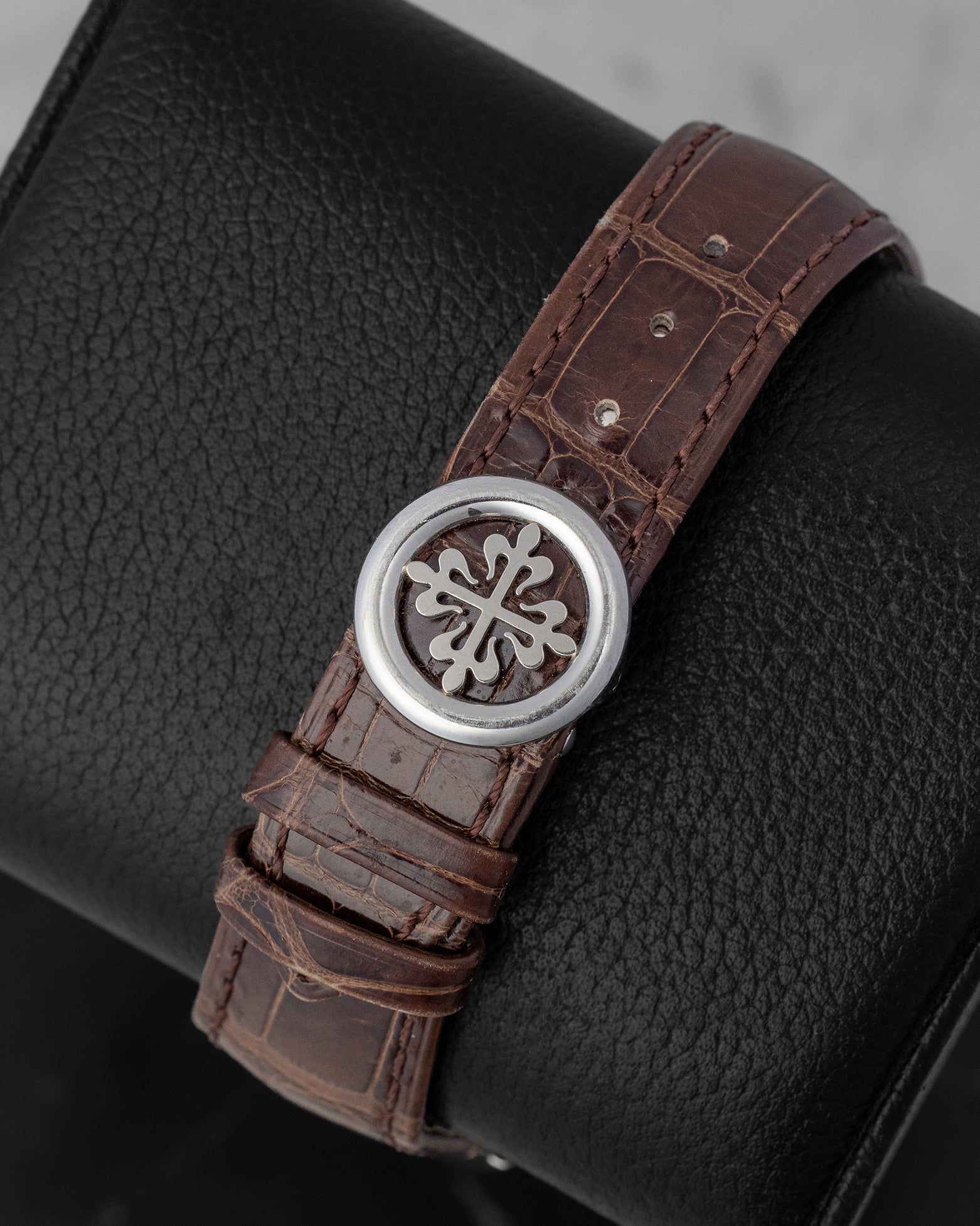 Close-up shot of the solid platinum foldover deployment clasp engraved with the iconic Patek Philippe Cross on a matte brown alligator strap