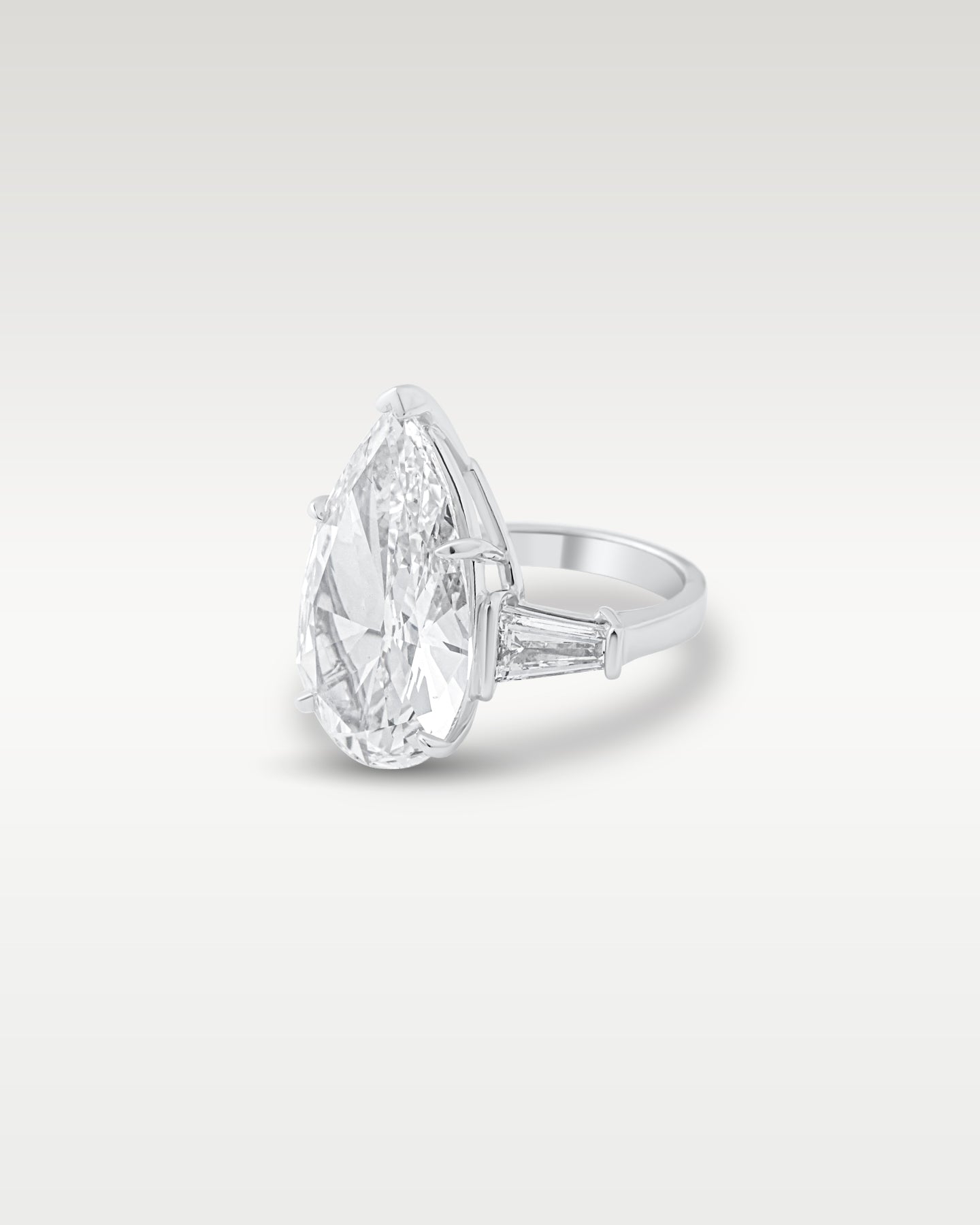 Three-quarter angle view showing the band detail and tapered baguette side stones on a platinum pear-cut diamond ring