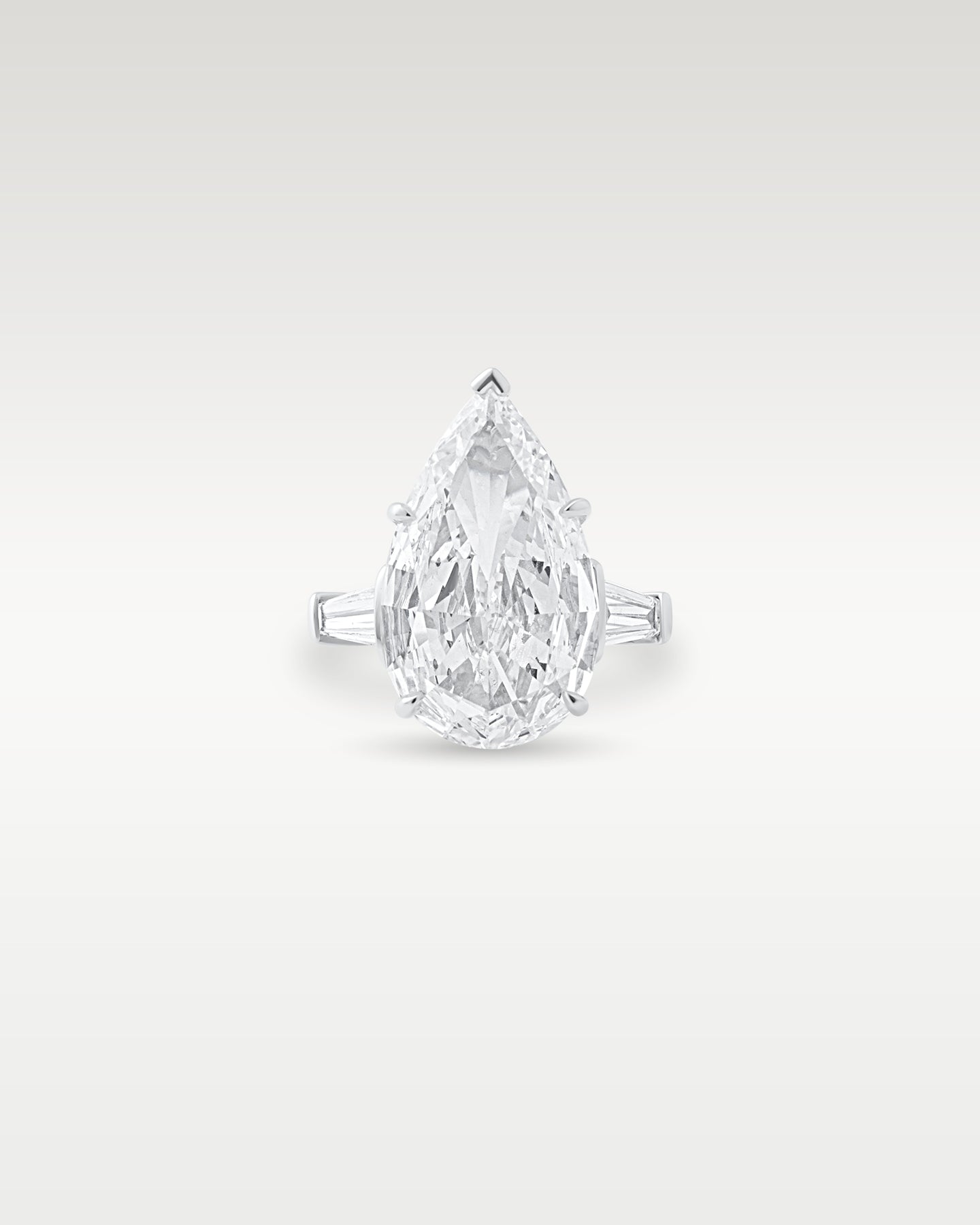 Front view of a platinum engagement ring featuring a large pear-cut diamond flanked by tapered baguette side stones from Noah's Fine Watches & Jewelry in Dallas, TX