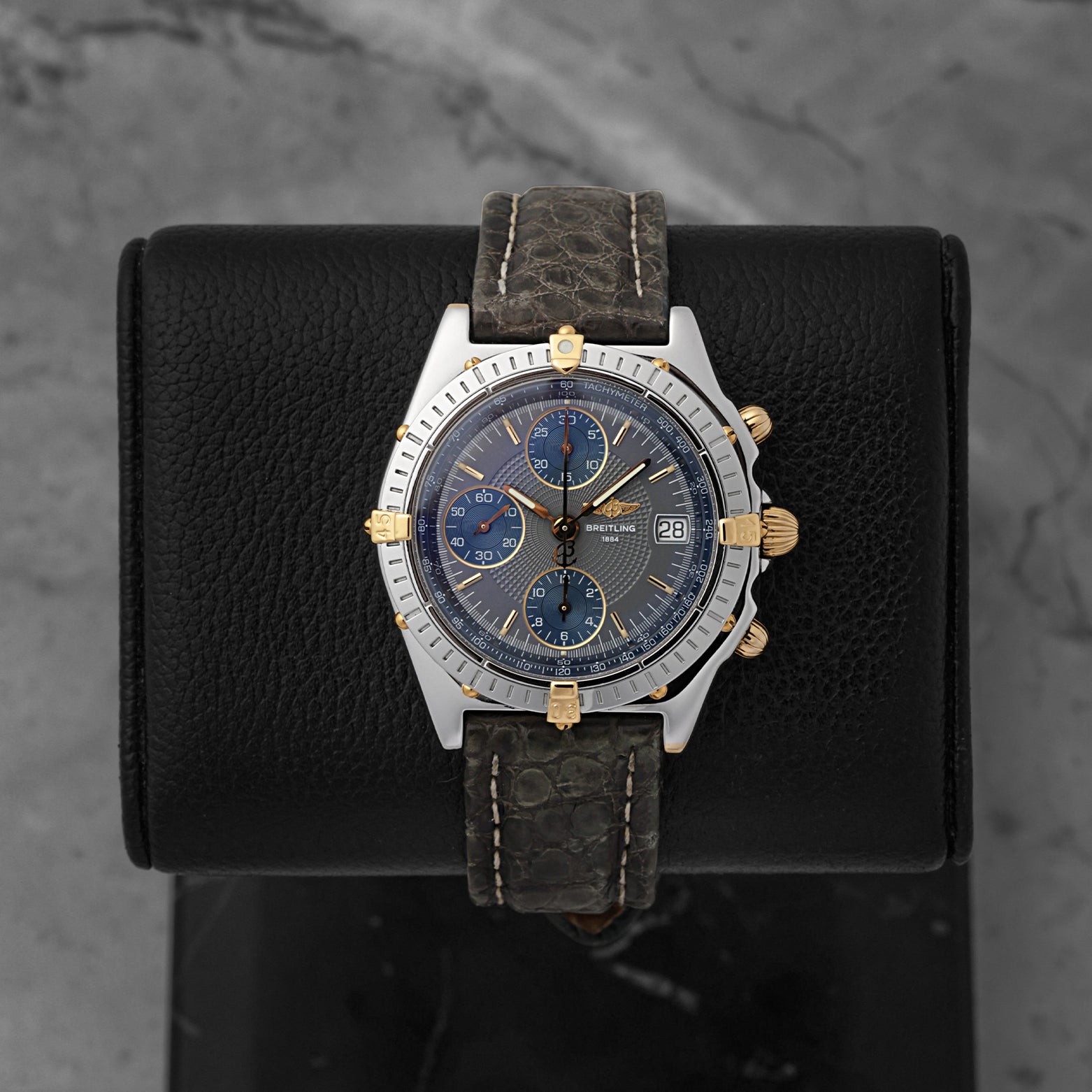 A preowned Breitling Chronomat reference B13050 in stainless steel and 18k yellow gold featuring a slate grey dial on a premium dark leather strap at Noah's Fine Watches & Jewelry in Dallas