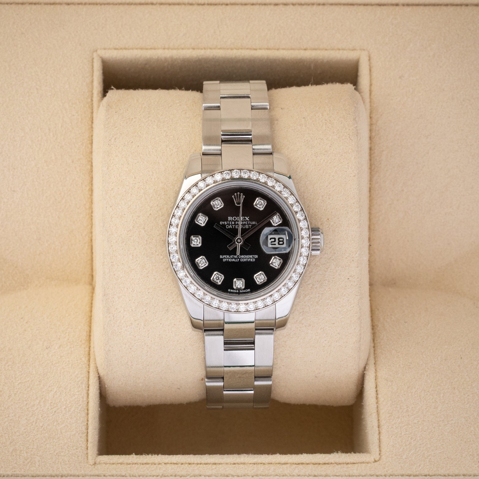 A ladies' pre-owned Rolex Lady-Datejust 26 reference 179384 featuring a black sunburst dial, factory diamond hour markers, and a diamond-set bezel inside its box at Noah's Fine Watches & Jewelry in Dallas