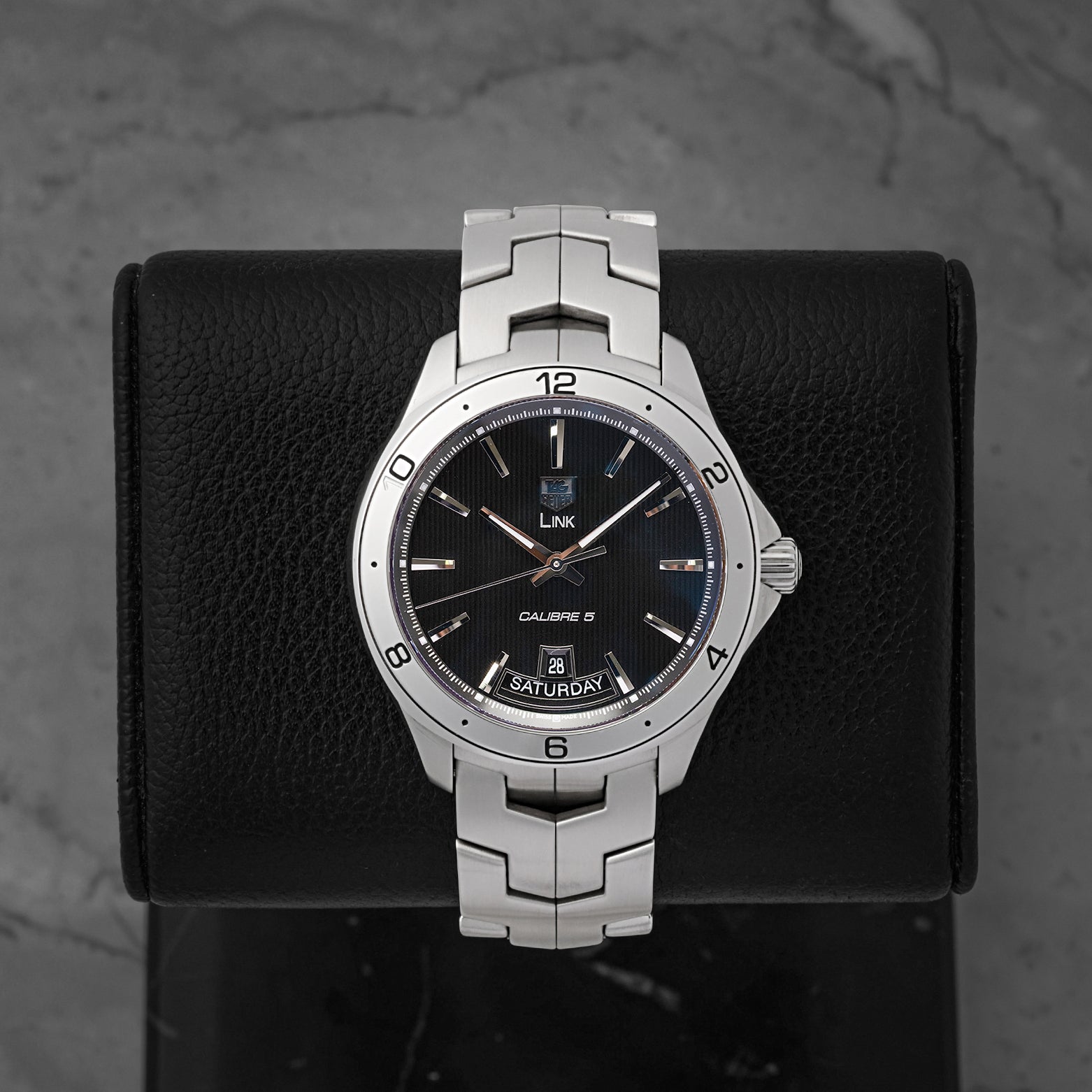A preowned TAG Heuer Link Calibre 5 Day-Date reference WAT2010 showing its black dial with vertical tuxedo pinstripes and unique 6 o'clock day-date window at Noah's Fine Watches & Jewelry in Dallas