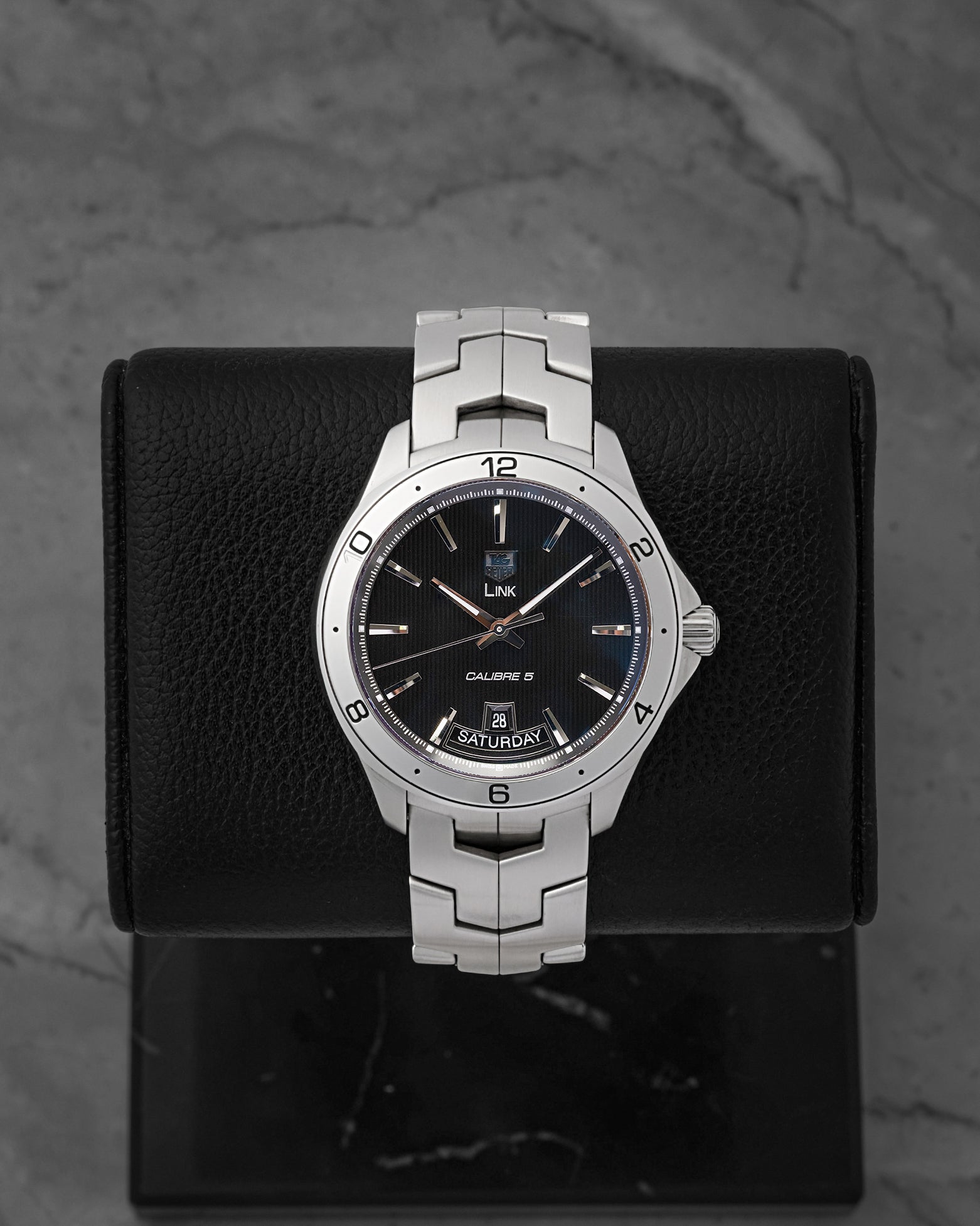 A preowned TAG Heuer Link Calibre 5 Day-Date reference WAT2010 showing its black dial with vertical tuxedo pinstripes and unique 6 o'clock day-date window at Noah's Fine Watches & Jewelry in Dallas