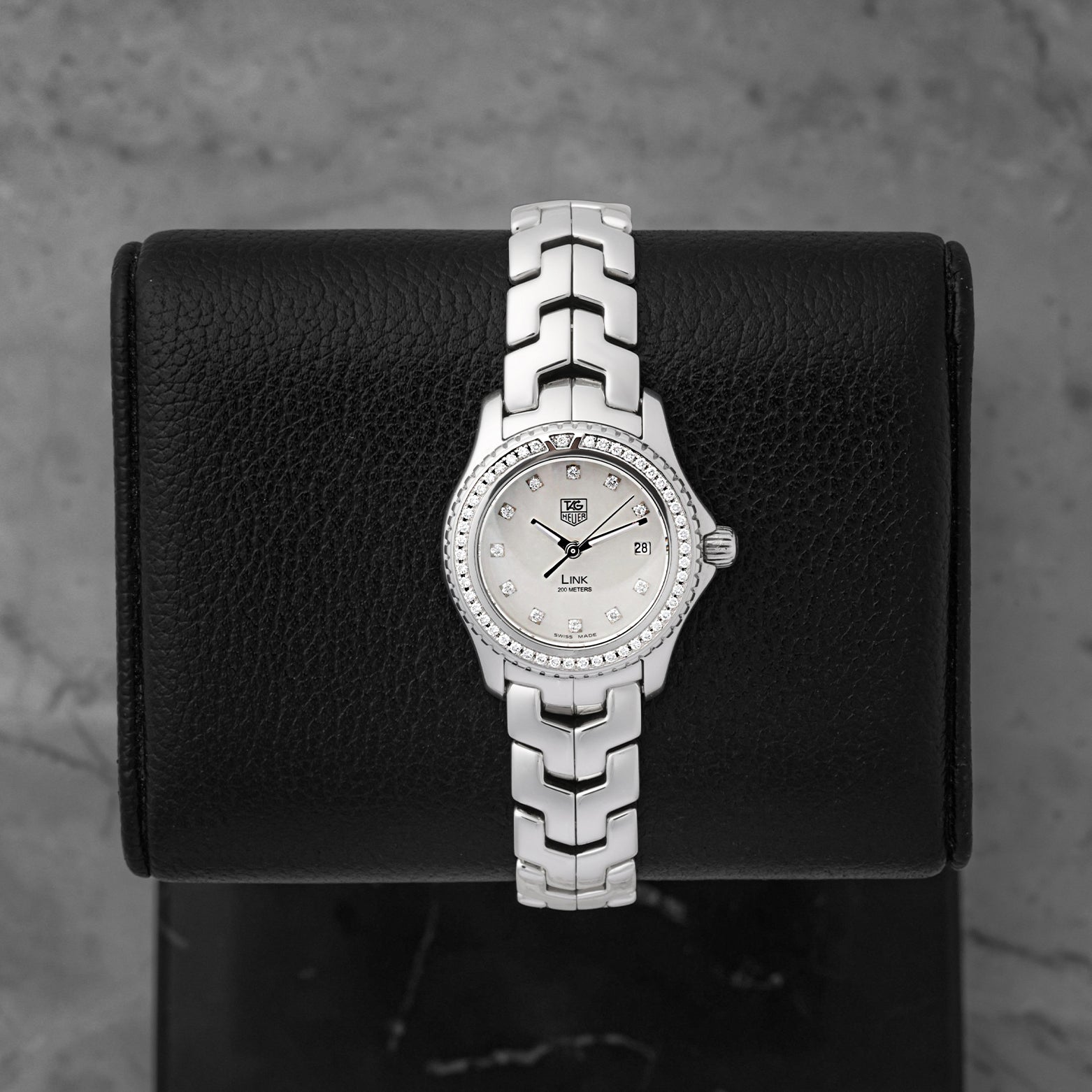 A ladies' pre-owned TAG Heuer Link reference WJF131A featuring an iridescent white mother-of-pearl dial with diamond hour markers and a diamond-set bezel at Noah's Fine Watches & Jewelry in Dallas
