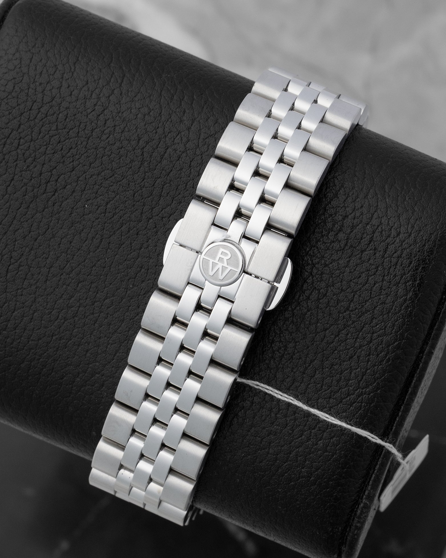 A five-link stainless steel watch bracelet with an integrated butterfly folding clasp showing the circular RW logo stamp