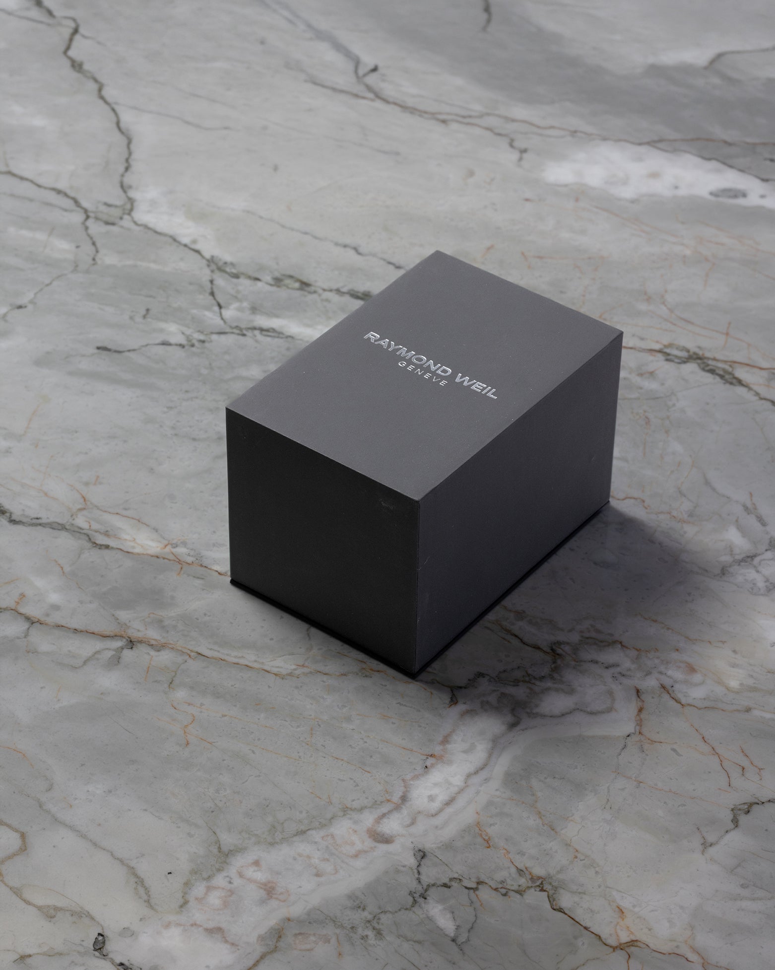 Original dark grey rectangular Raymond Weil luxury watch presentation storage box resting on a grey marble table
