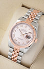 An angled studio profile view of a two-tone steel and 18k rose gold Rolex Datejust 36 watch on a cream display cushion
