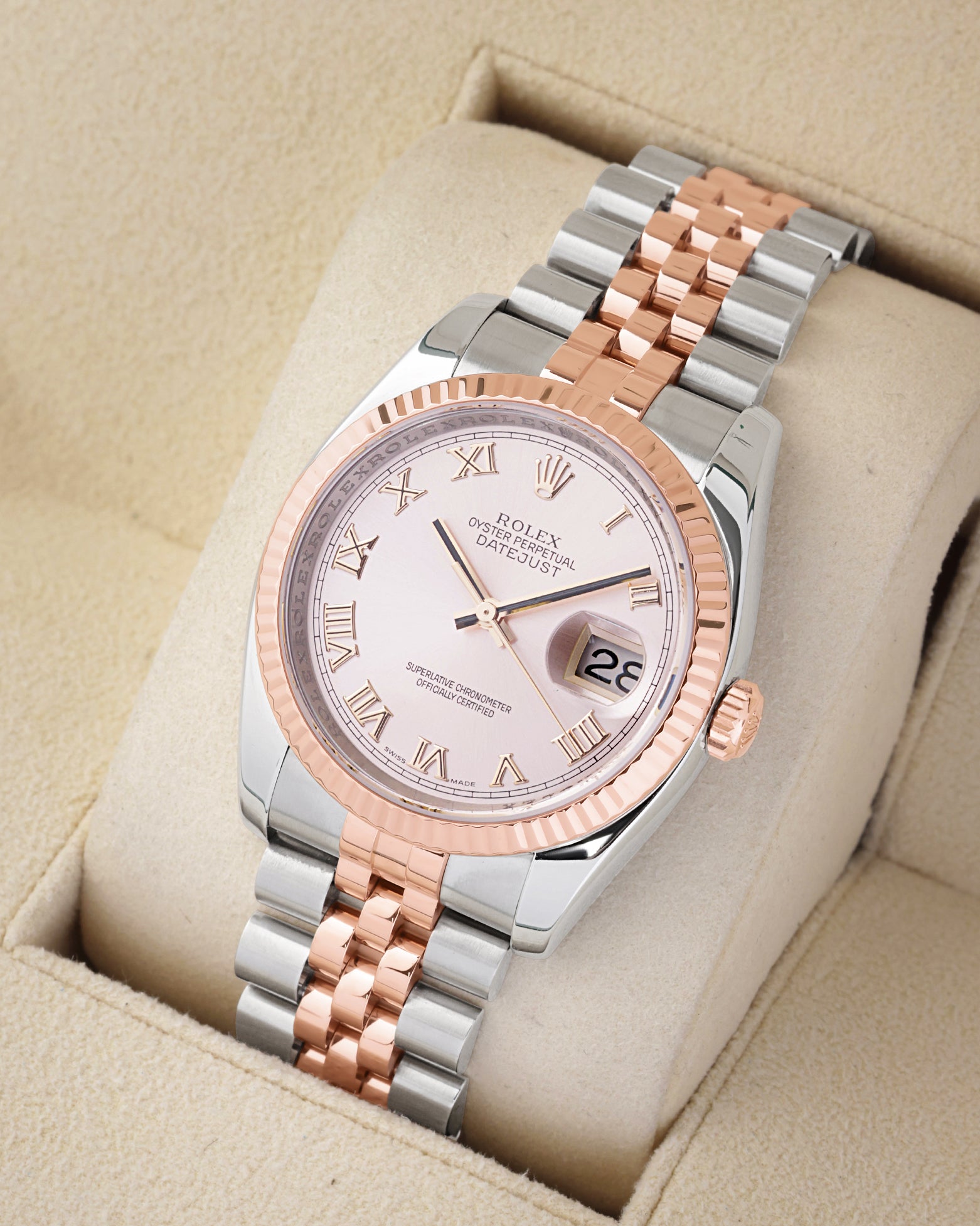An angled studio profile view of a two-tone steel and 18k rose gold Rolex Datejust 36 watch on a cream display cushion