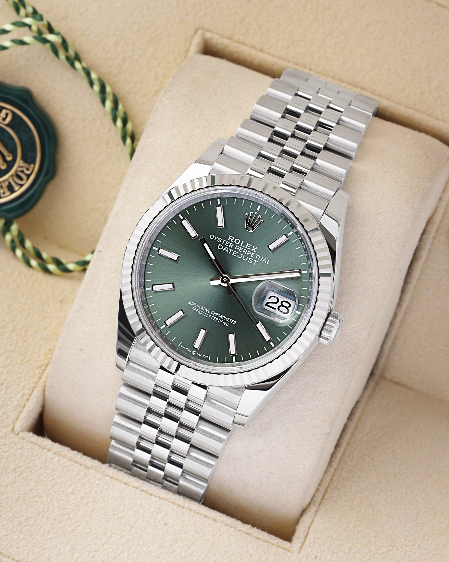An angled studio profile view of the stainless steel Rolex Datejust 36 mint green dial watch resting on a cream display cushion