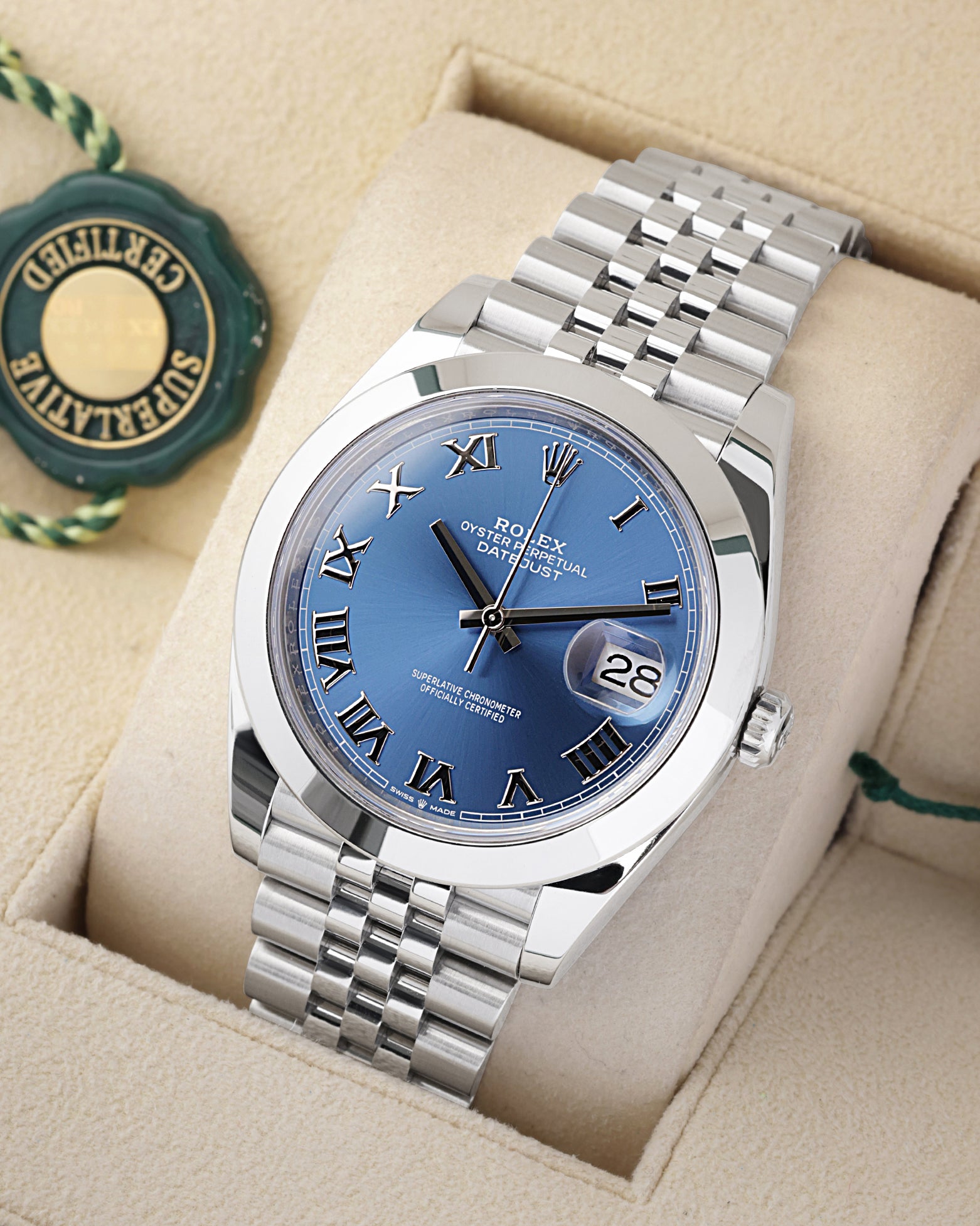 An angled studio profile view of a stainless steel Rolex Datejust 41 watch resting on a cream display cushion