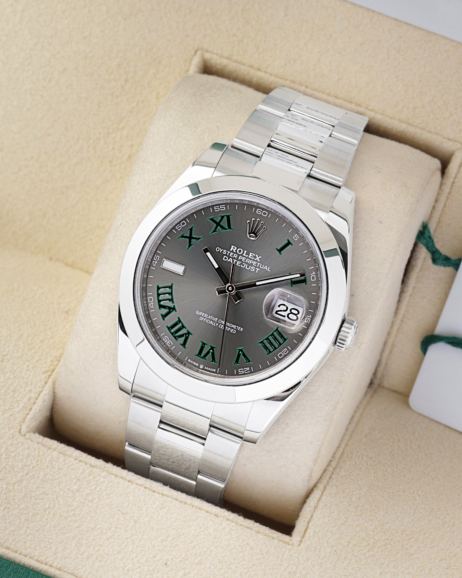 An angled studio profile view of a stainless steel 41mm Rolex Datejust Wimbledon watch resting on a cream display cushion
