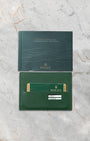 Official green Rolex international guarantee card resting below its matching green user operating manual manual booklet on a marble surface