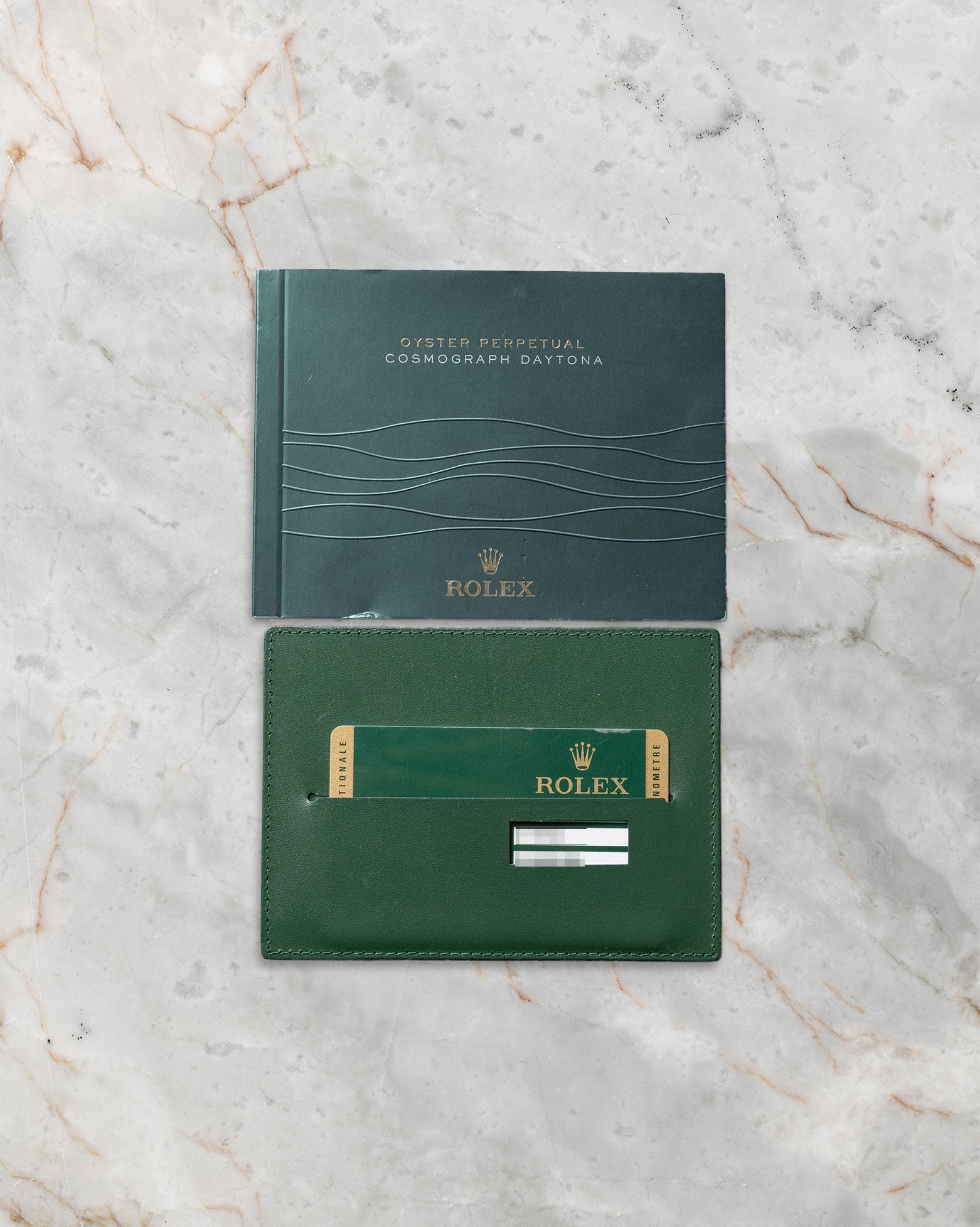 Official green Rolex international guarantee card resting below its matching green user operating manual manual booklet on a marble surface