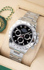 angled profile view of a pre-owned steel Rolex Daytona reference 116520 showcasing the black racing dial on its presentation cushion