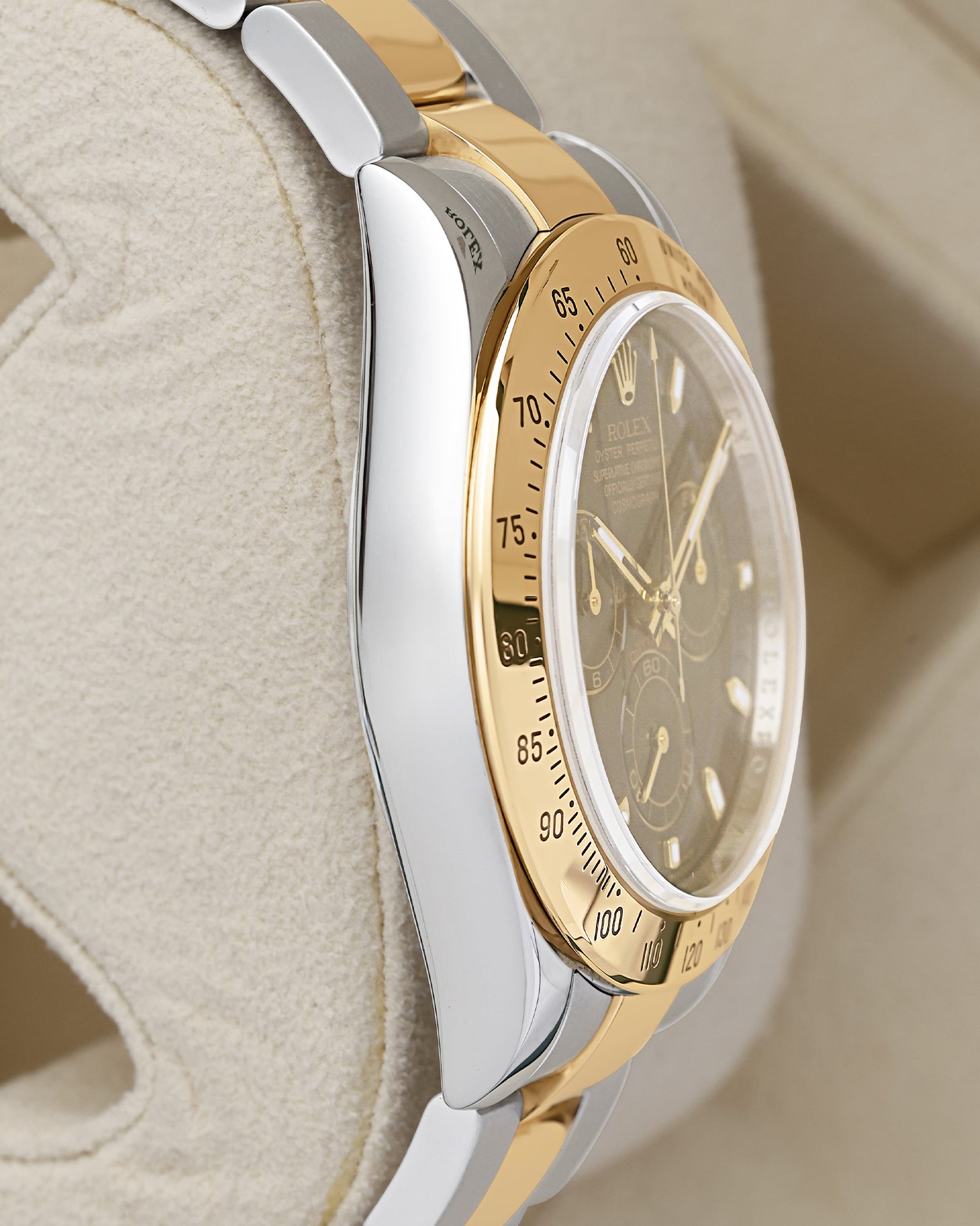 left-side case profile view of a pre-owned two-tone 40mm stainless steel and 18k gold Rolex Daytona Oyster case resting on a cushion