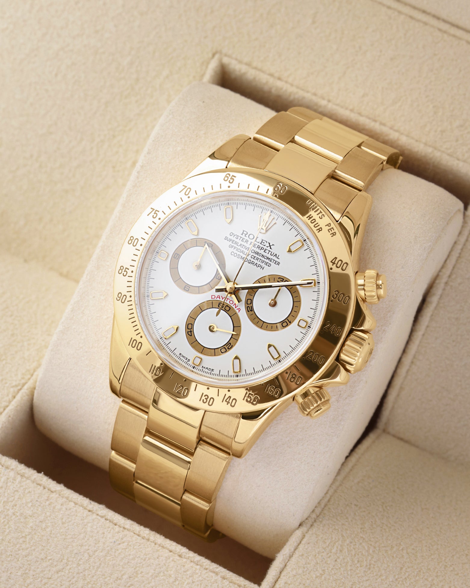 An angled studio profile shot of the heavy 18k yellow gold case and Oyster bracelet of a Rolex Daytona 116528 resting on a cream cushion
