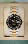 Front portrait view of a pre-owned 2004 Rolex GMT-Master II Ref 16713 two-tone yellow Rolesor watch with a black index dial, on display at Noahs Fine Watches and Jewelry Dallas
