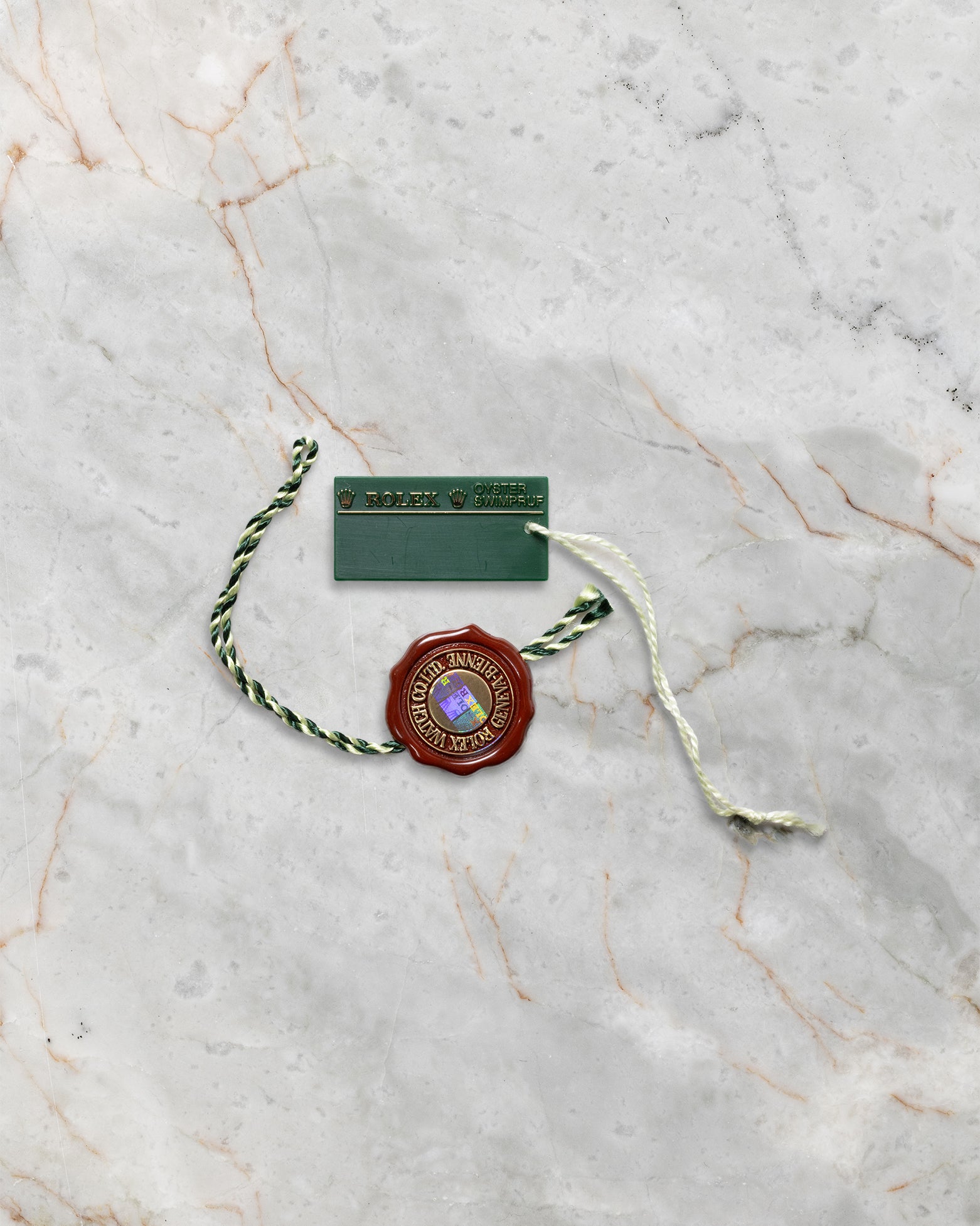 Official green holographic Rolex Superlative Chronometer string seal tag and white serialized pricing hang tag on marble