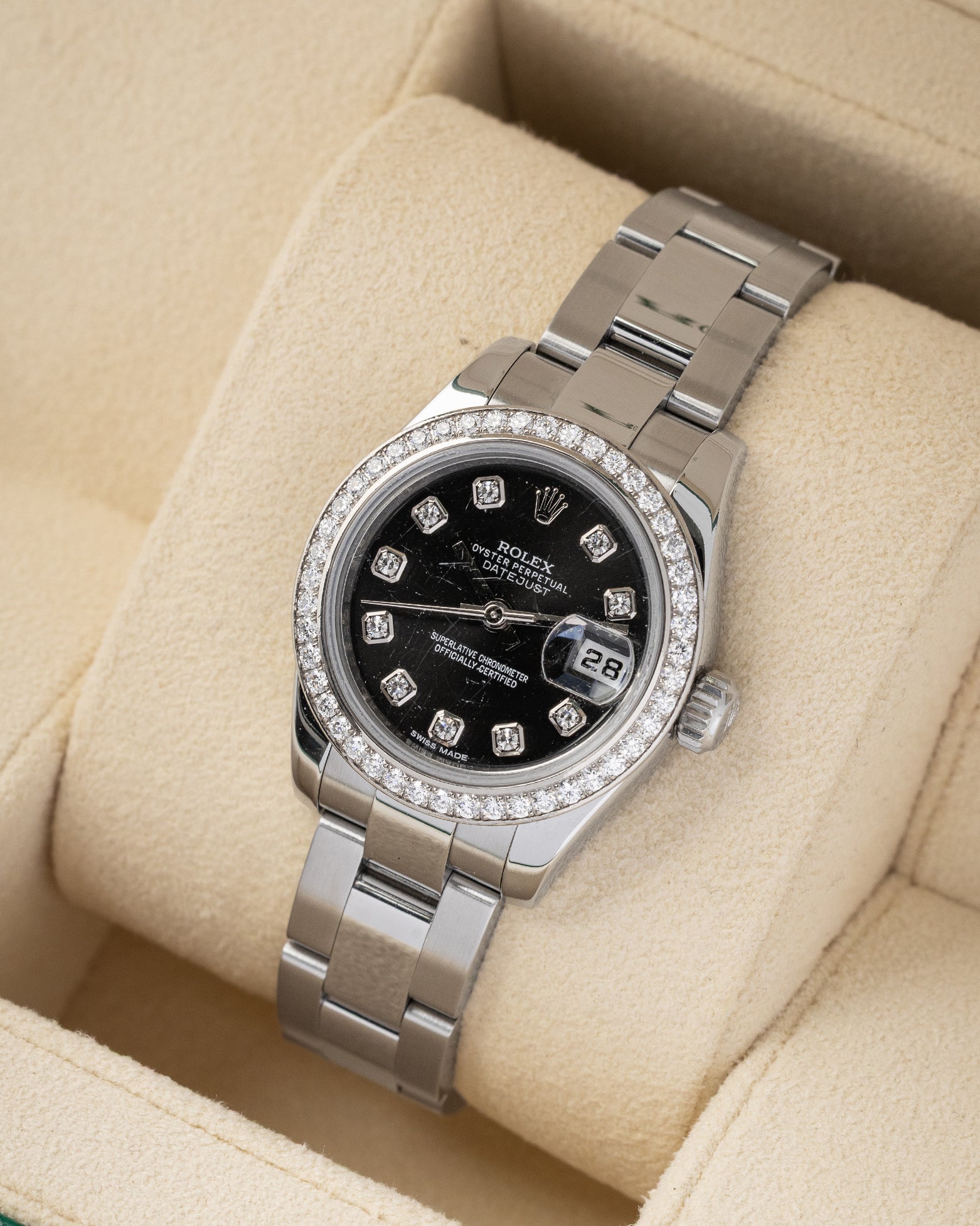 angled overhead view of the 26mm steel and white gold Rolex Lady-Datejust watch with a diamond bezel resting on a beige leather watch cushion