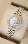 An angled studio profile shot of a two-tone steel and gold Rolex Lady-Datejust 26mm watch resting on a cream display cushion
