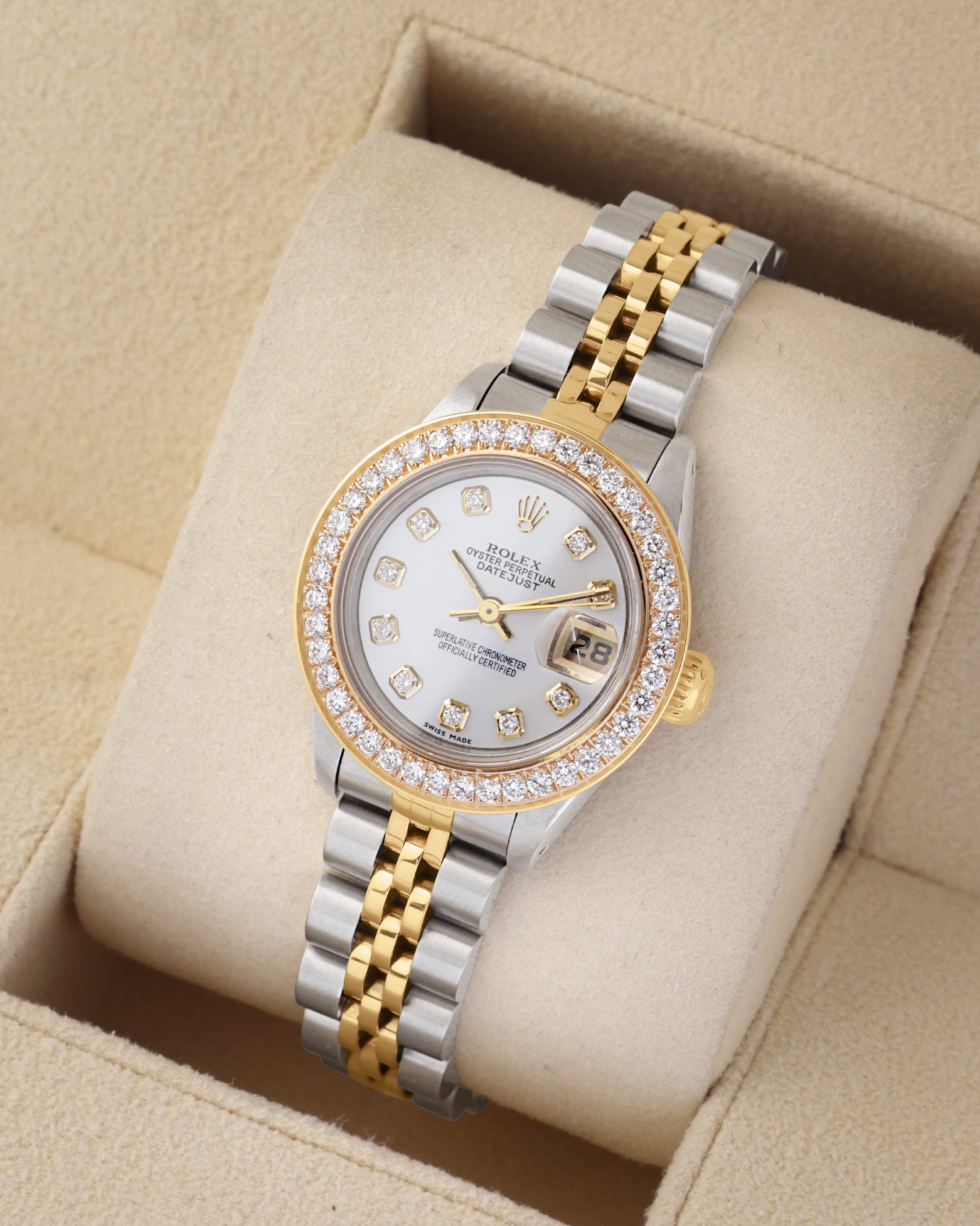 An angled studio profile shot of a two-tone steel and gold Rolex Lady-Datejust 26mm watch resting on a cream display cushion