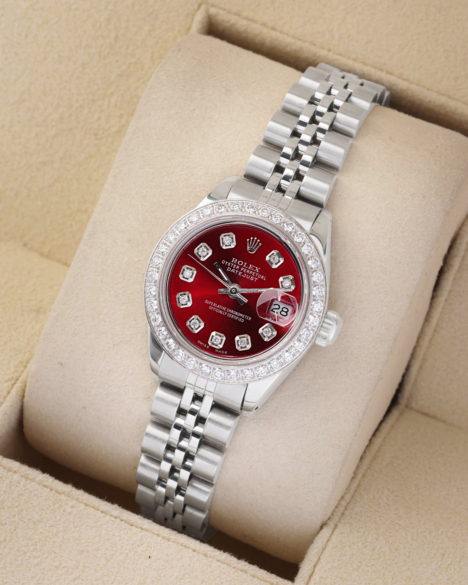 An angled studio view of a stainless steel 26mm Rolex Lady-Datejust watch resting on a cream display cushion