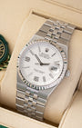 A high-angle three-quarter studio portrait of the 36mm Rolex Land-Dweller showcasing the seamless fluid transition from the case to the flat five-piece link bracelet on a beige cushion