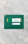 The official green Rolex leather cardholder wallet displaying the plastic international warranty card flat on a marble surface