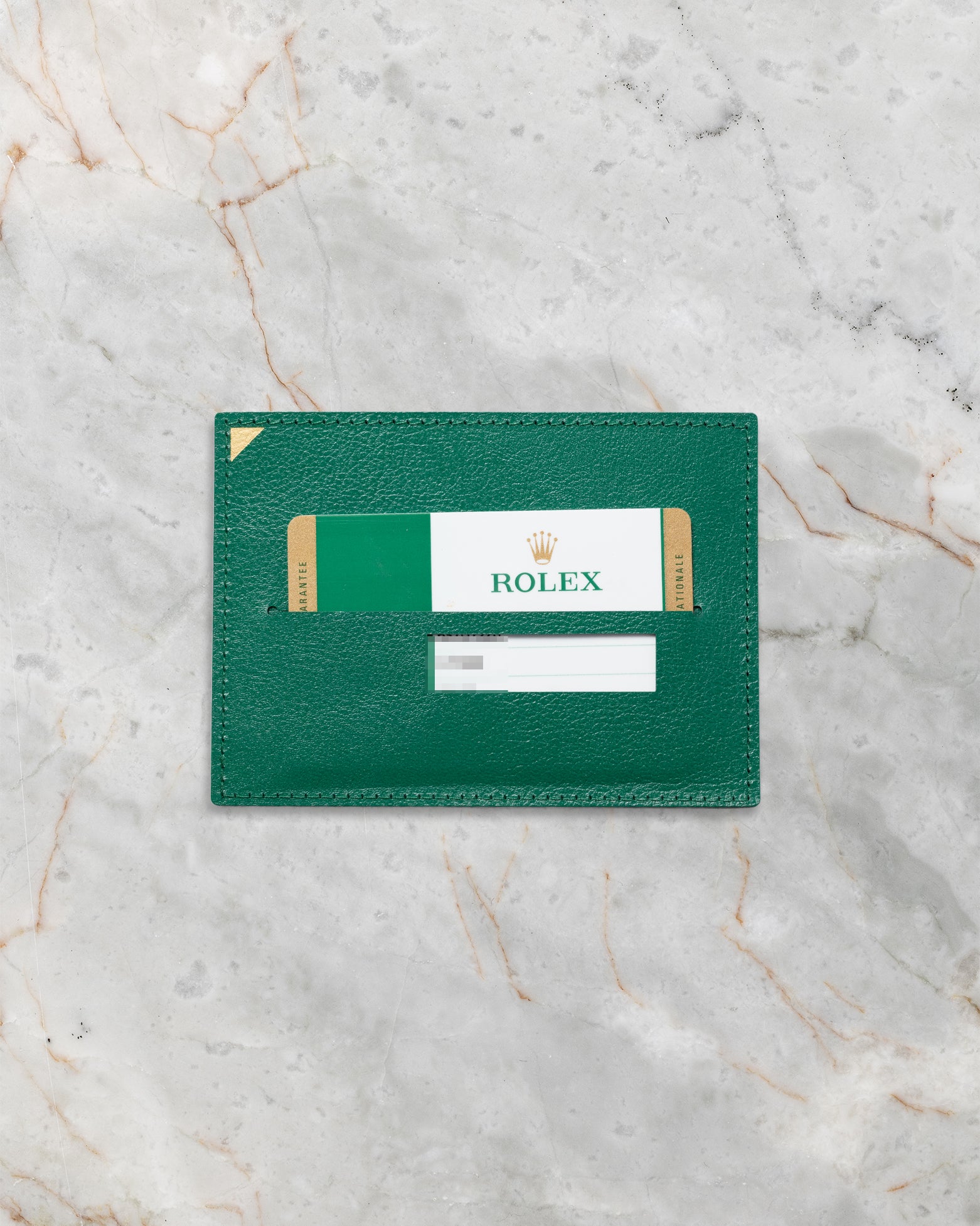 The official green Rolex leather cardholder wallet displaying the plastic international warranty card flat on a marble surface