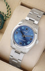 An angled studio profile shot of the stainless steel midsize 31mm Rolex Oyster Perpetual watch on a cream display cushion