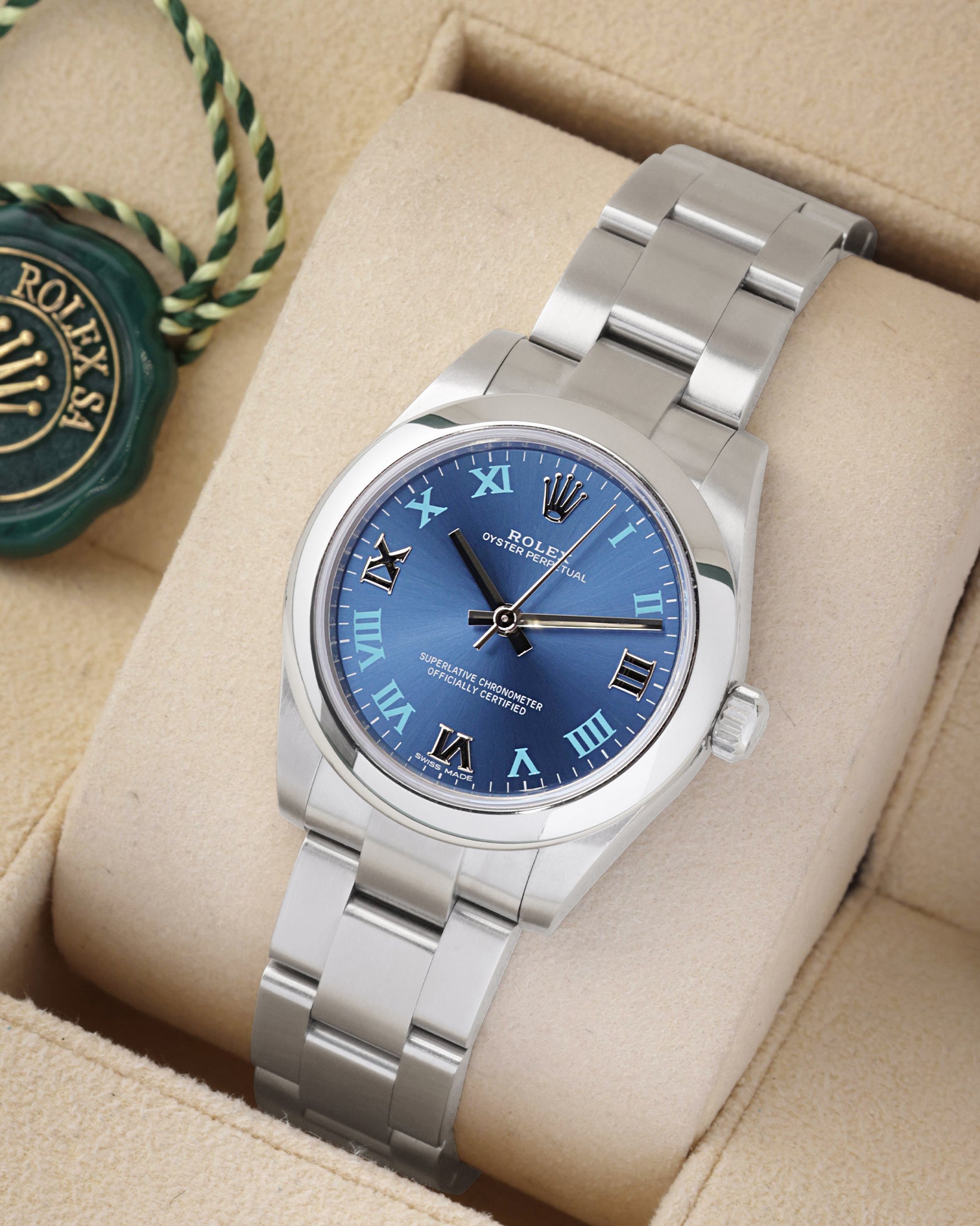 An angled studio profile shot of the stainless steel midsize 31mm Rolex Oyster Perpetual watch on a cream display cushion