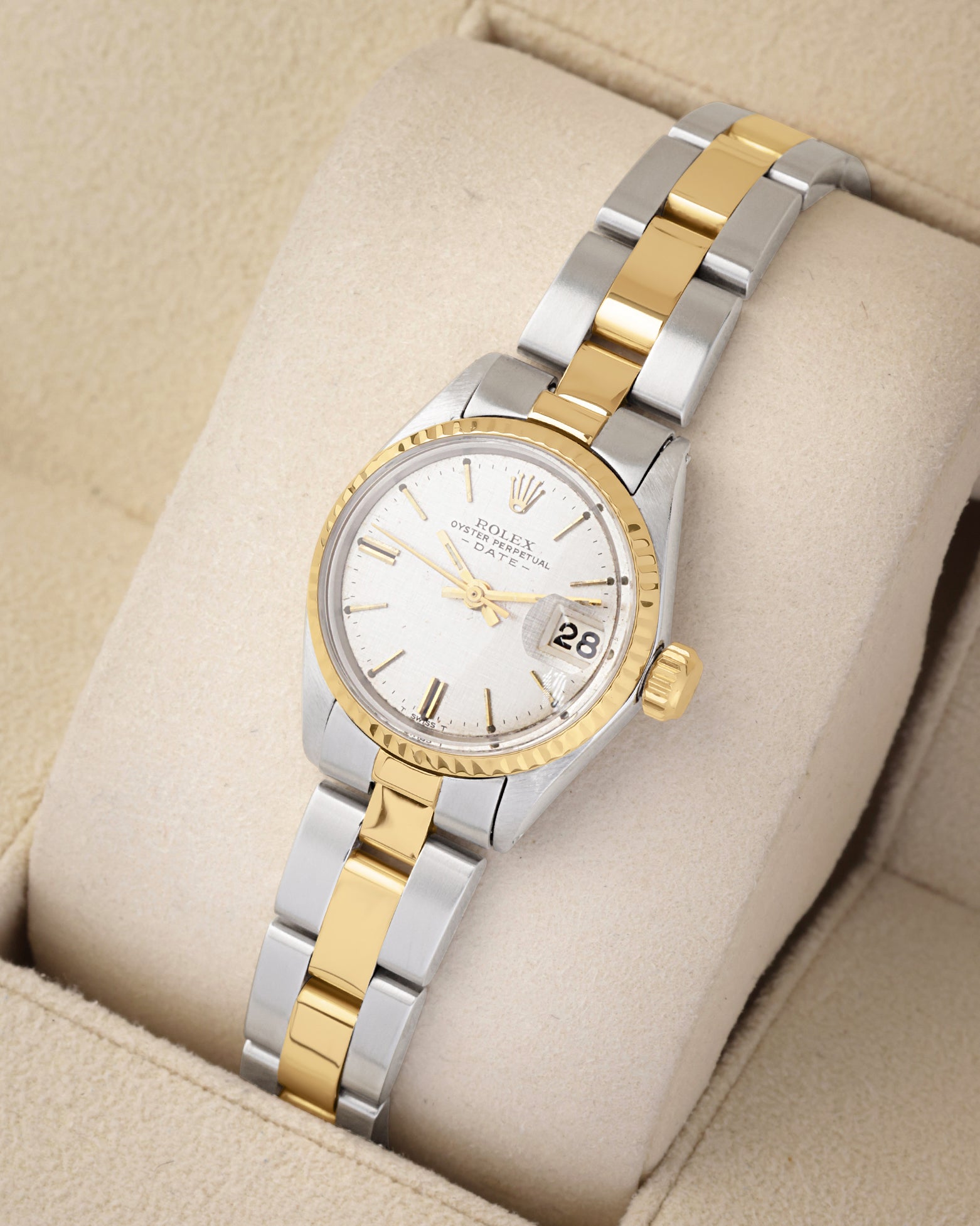 An angled studio profile shot of a 1969 two-tone Rolex Oyster Perpetual Date watch on a cream velvet cushion