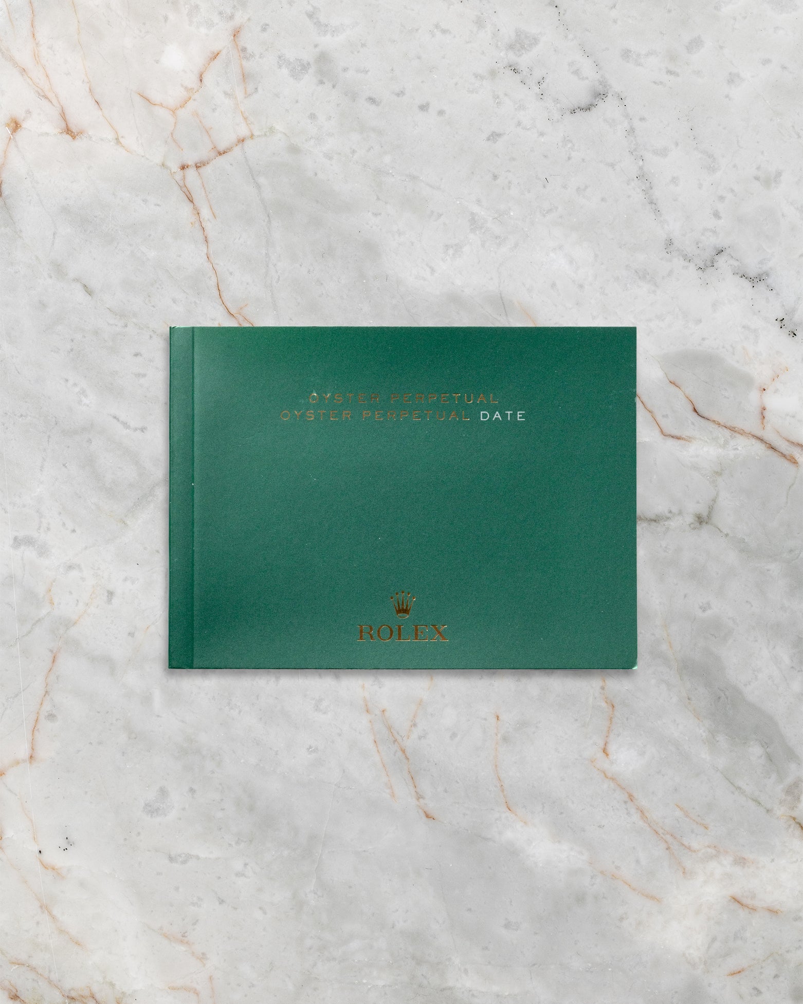 The official green Rolex Oyster Perpetual user guide booklet and instruction documentation laid flat on a gray marble background