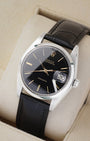 An angled studio profile shot of the stainless steel case and black leather strap of a vintage Rolex Oysterdate 6694 watch