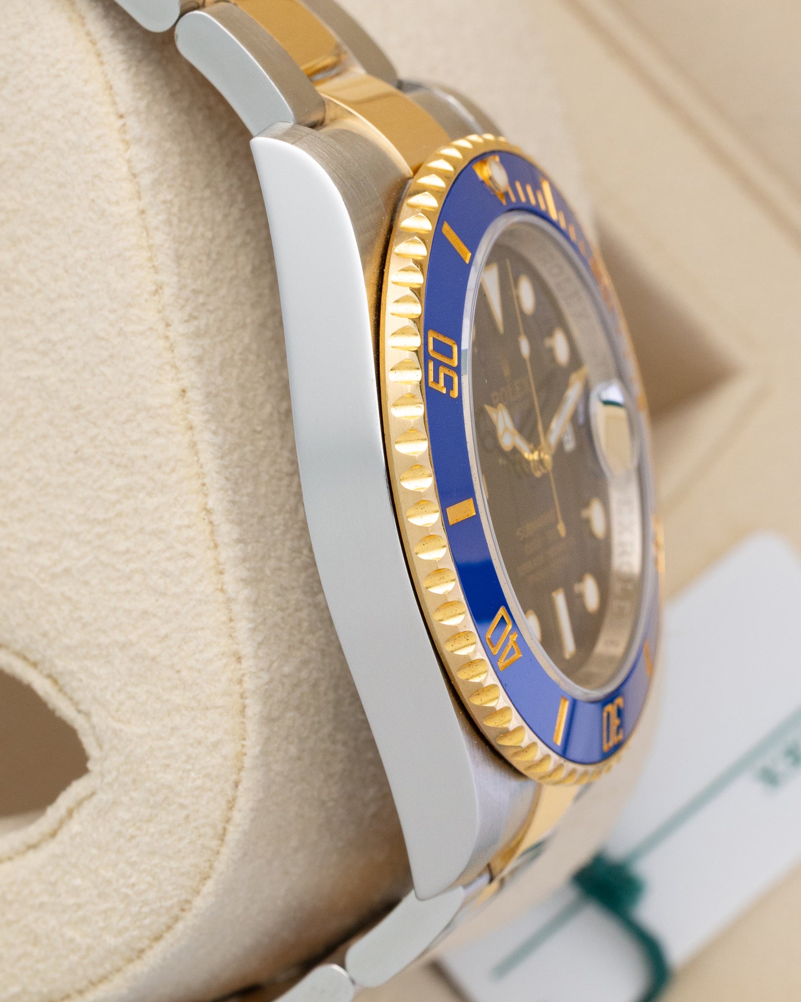 Left side profile view of the polished stainless steel case and 18k yellow gold blue ceramic bezel edge on a preowned 2018 Rolex Submariner 116613LB