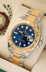 angled top-down overview of the 40mm yellow gold and steel Rolex Yacht-Master watch with a blue dial resting on its tan leather cushion