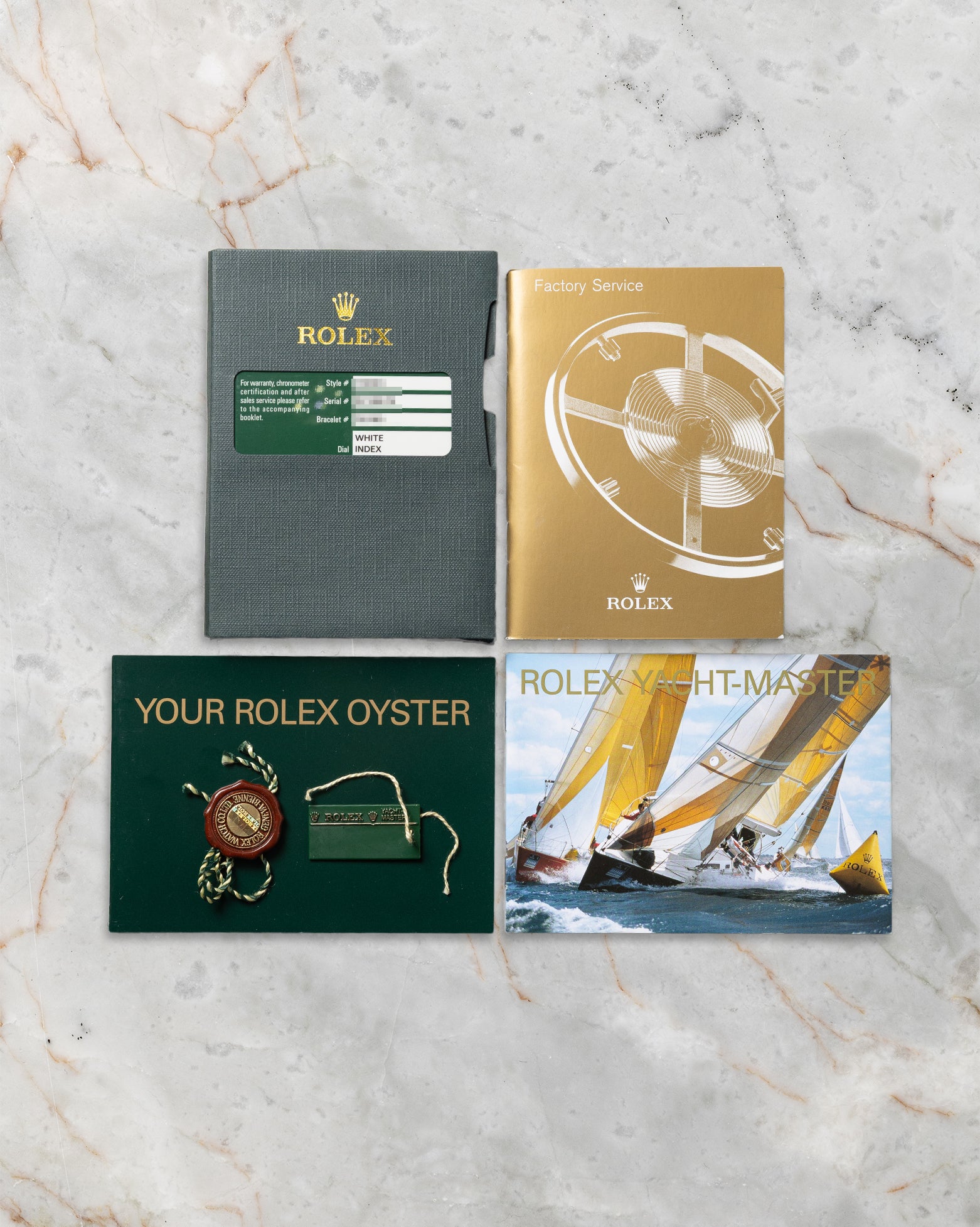 top-down flat-lay view of the green Rolex warranty card, Yacht-Master instruction manual, and official collateral paperwork on marble