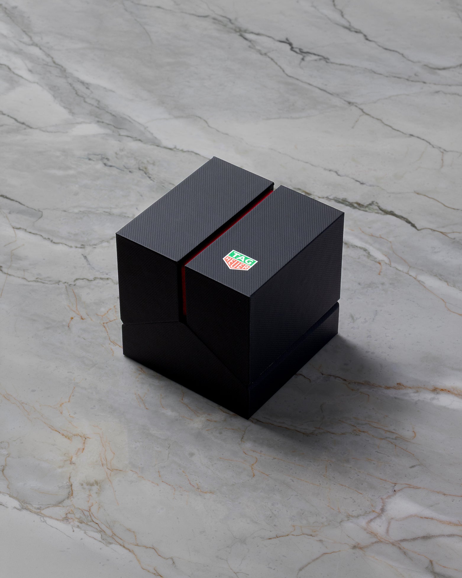 closed modern matte black TAG Heuer luxury watch presentation box featuring a green shield logo accent split on a gray marble background