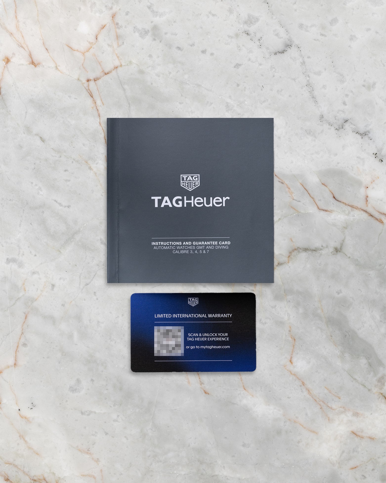 Official dark grey TAG Heuer international guarantee card displayed on marble below its matching brand instruction and service history manual booklet