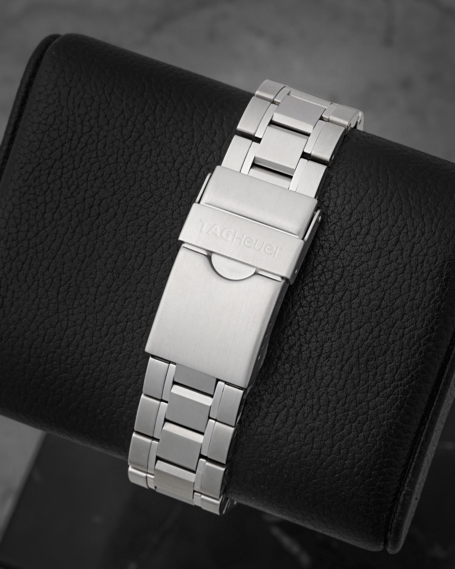 A rear view of the flat three-row sports link metal band focusing on the secure fold-over safety latch deployant buckle stamped with the historical TAG Heuer block text