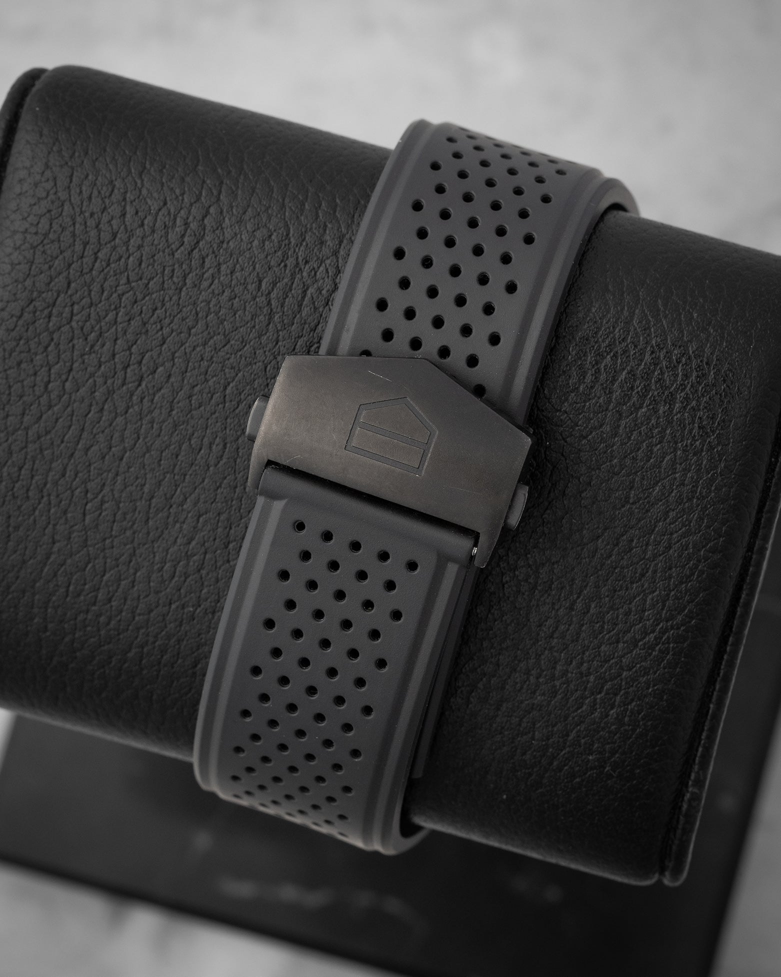 rear snapshot focusing on the perforated black rubber racing strap and the dark titanium folding deployment buckle featuring the Heuer shield