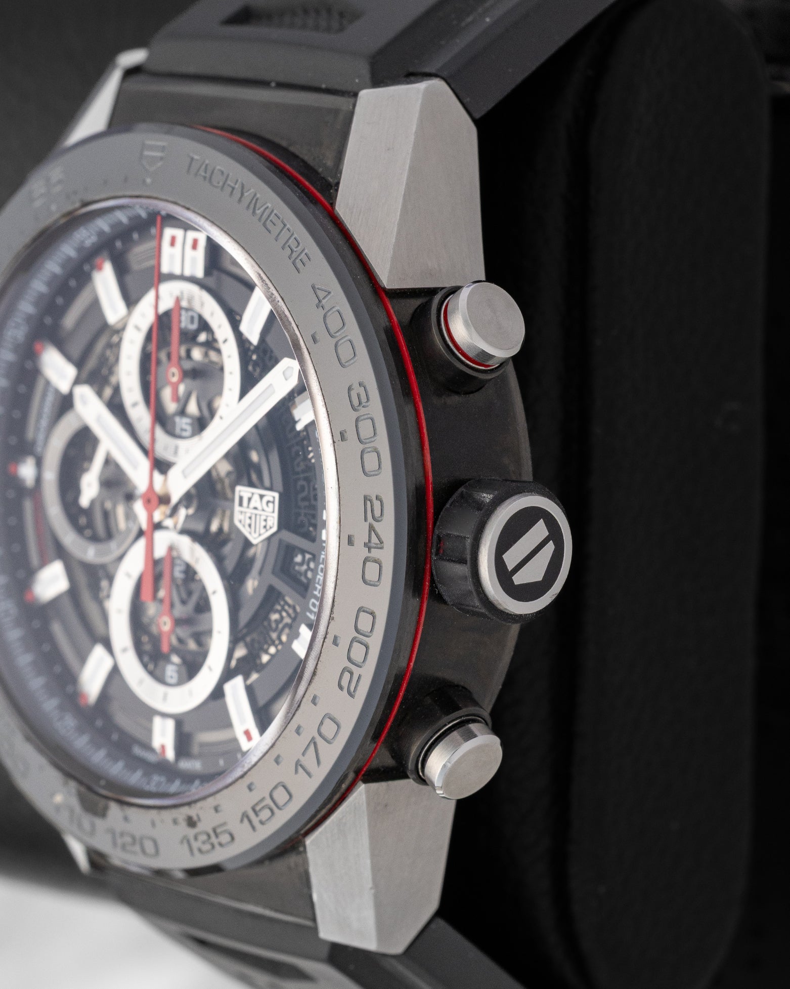 Close-up right profile view of the 45mm titanium Carrera case showing the red-accented chronograph pushers and rubber-gripped crown