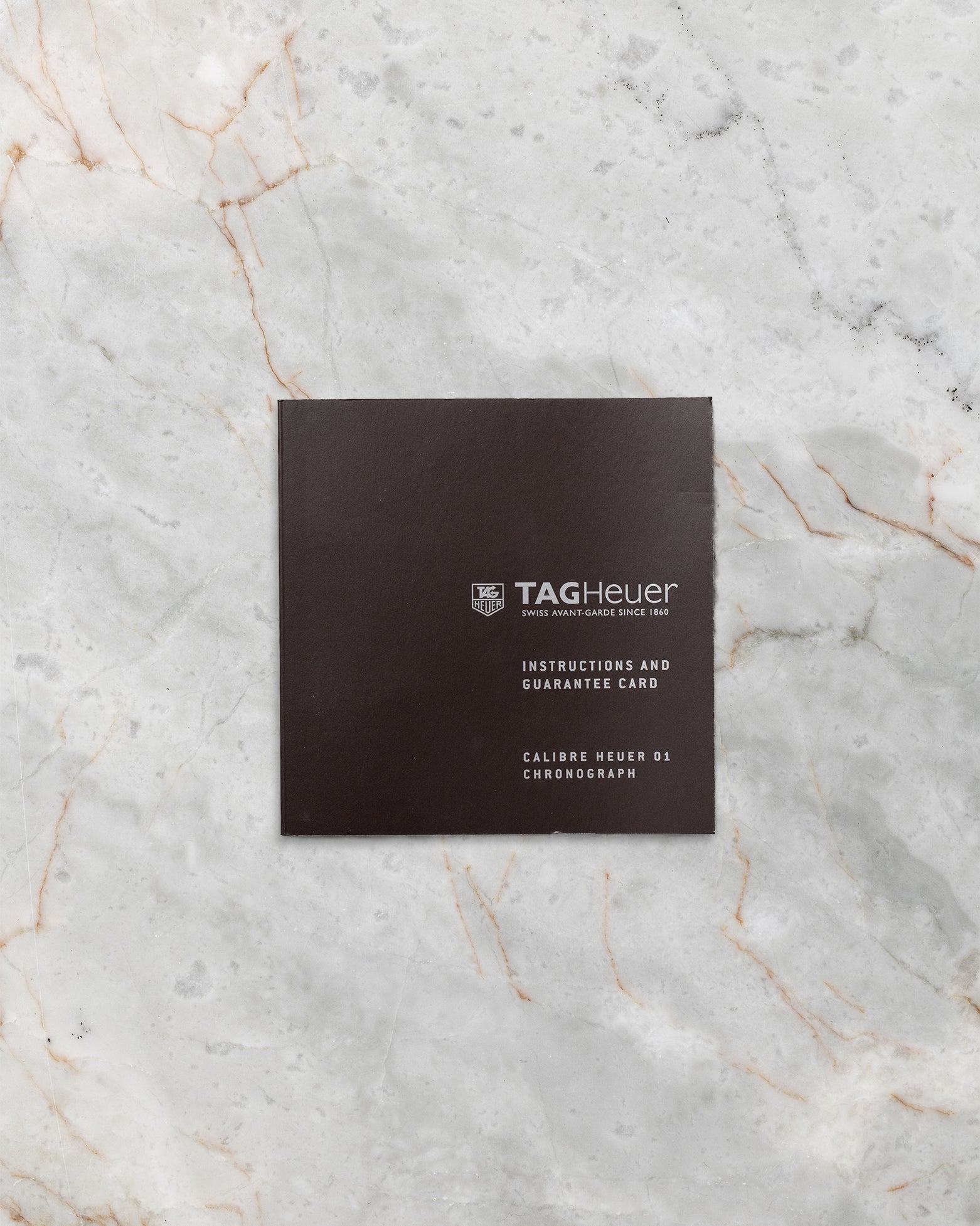 dark textured TAG Heuer official user instruction booklet and service documentation resting flat on a white marble background