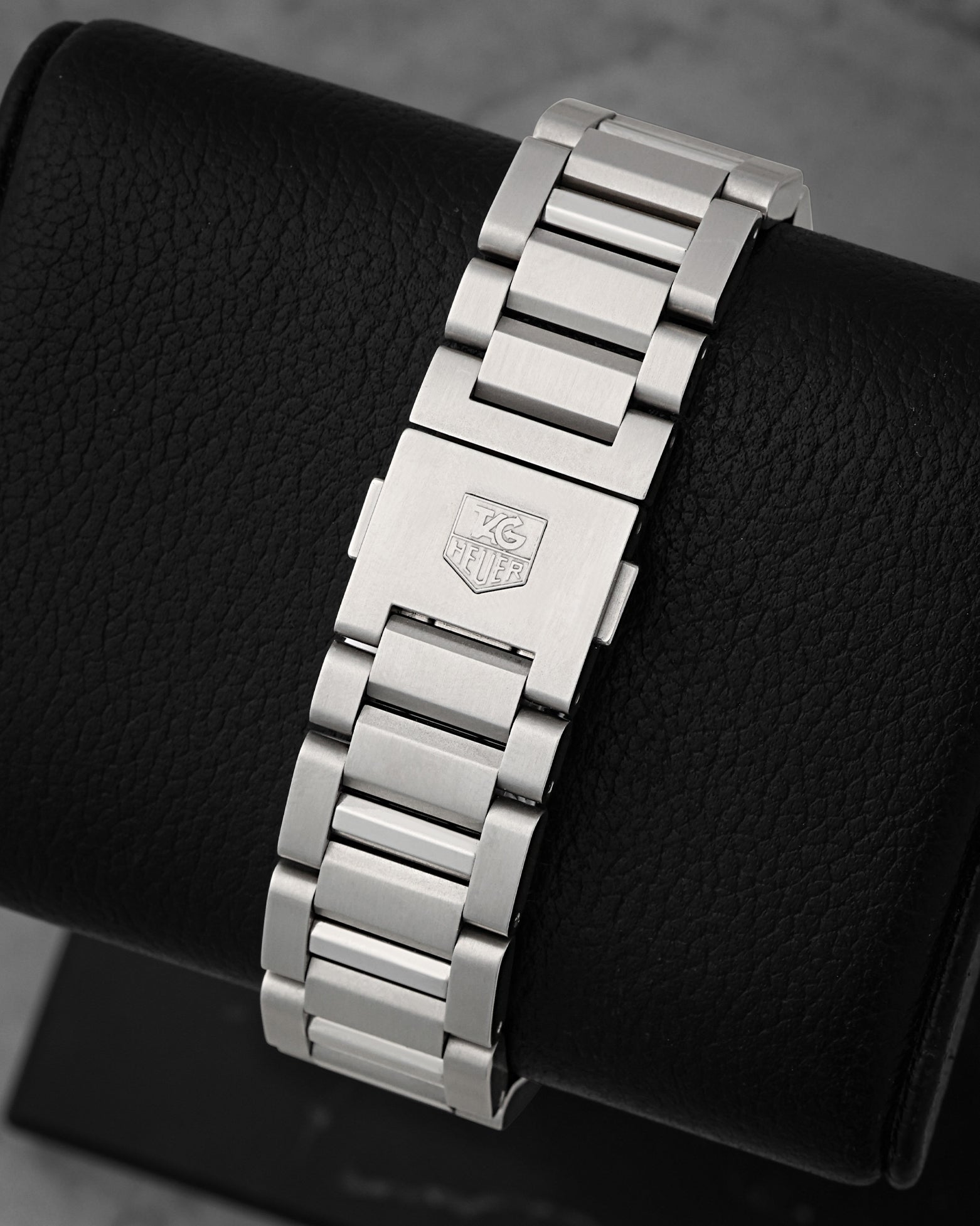 A rear view of the three-row stainless steel H-link metal watch band focusing on the secure push-button folding deployment clasp engraved with the block brand crest logo