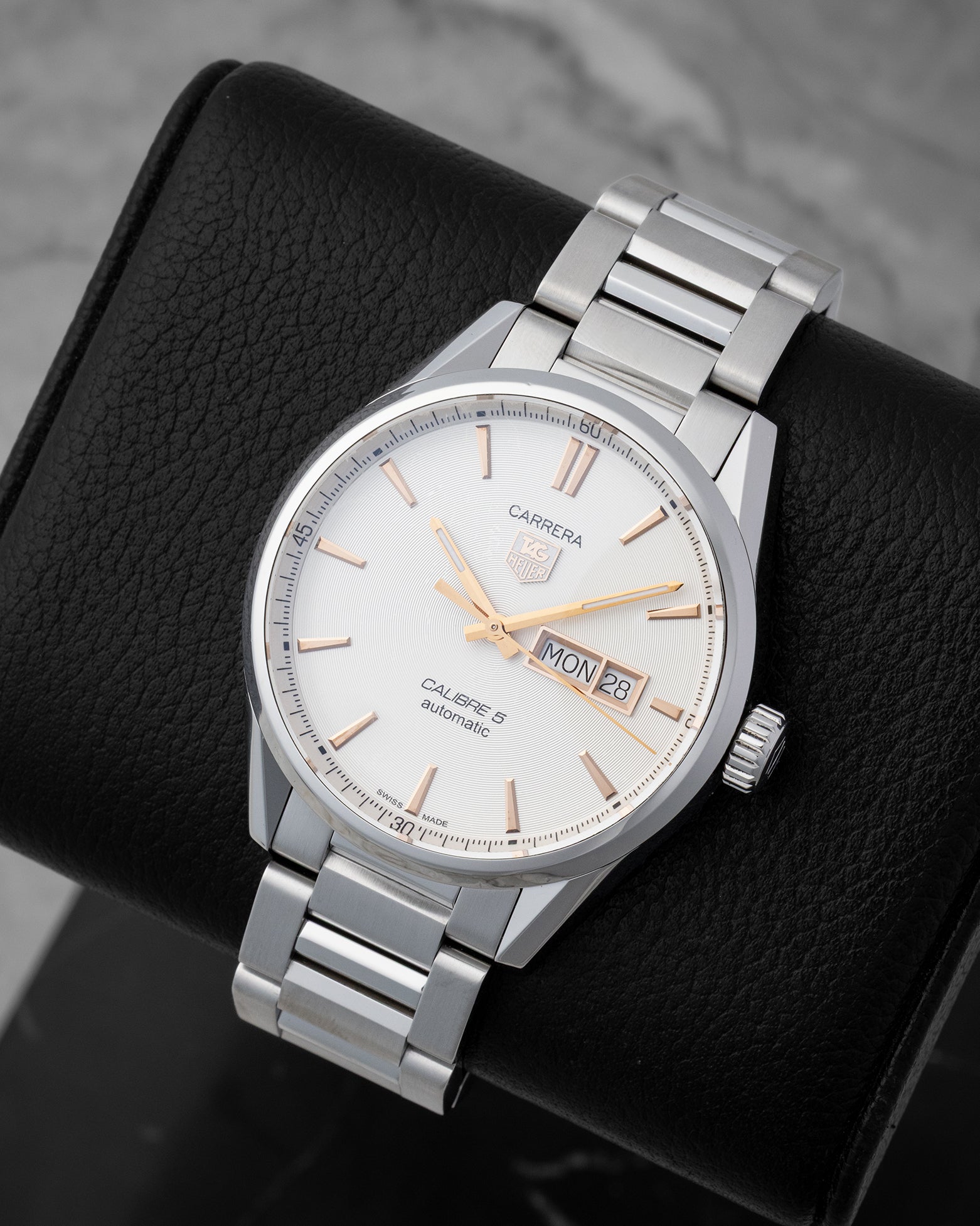An angled studio view of the TAG Heuer Carrera Calibre 5 automatic watch resting on a black leather display cushion