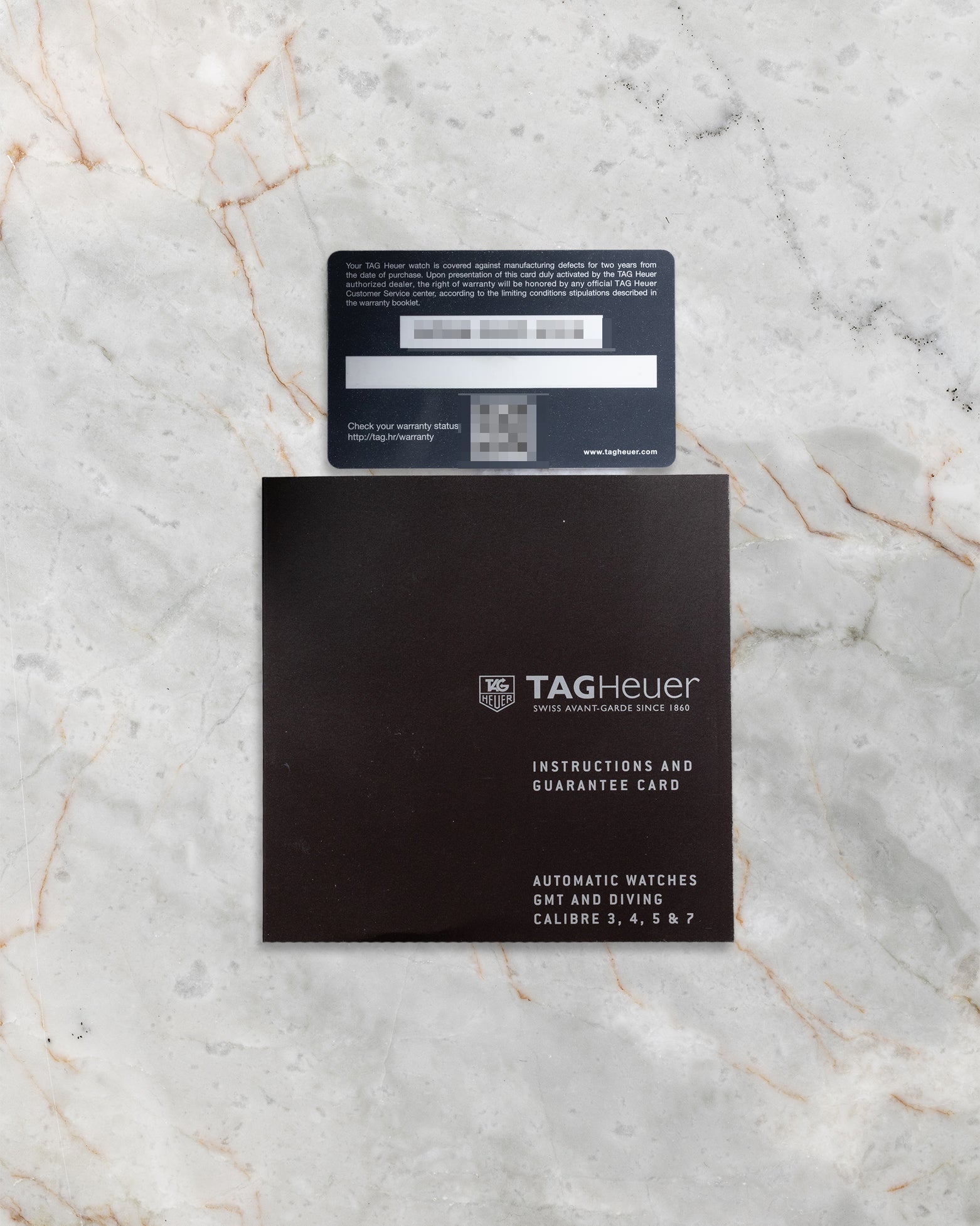 The official TAG Heuer international warranty card and black user manual paperwork laid flat on a marble background